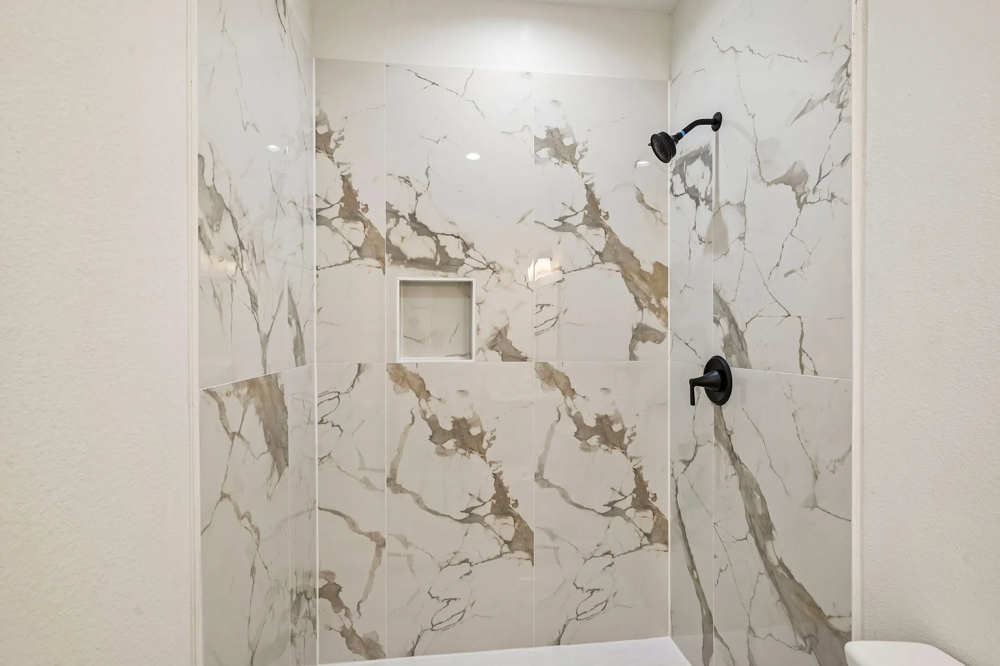 Shower featuring large format tile with naturalistic veining, a built-in niche, and matte black fixtures