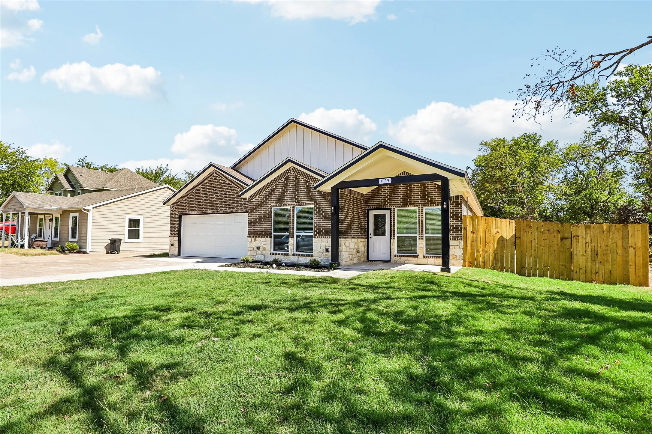 Brick and stone exterior with a covered entry, attached garage, and a wood privacy fence
