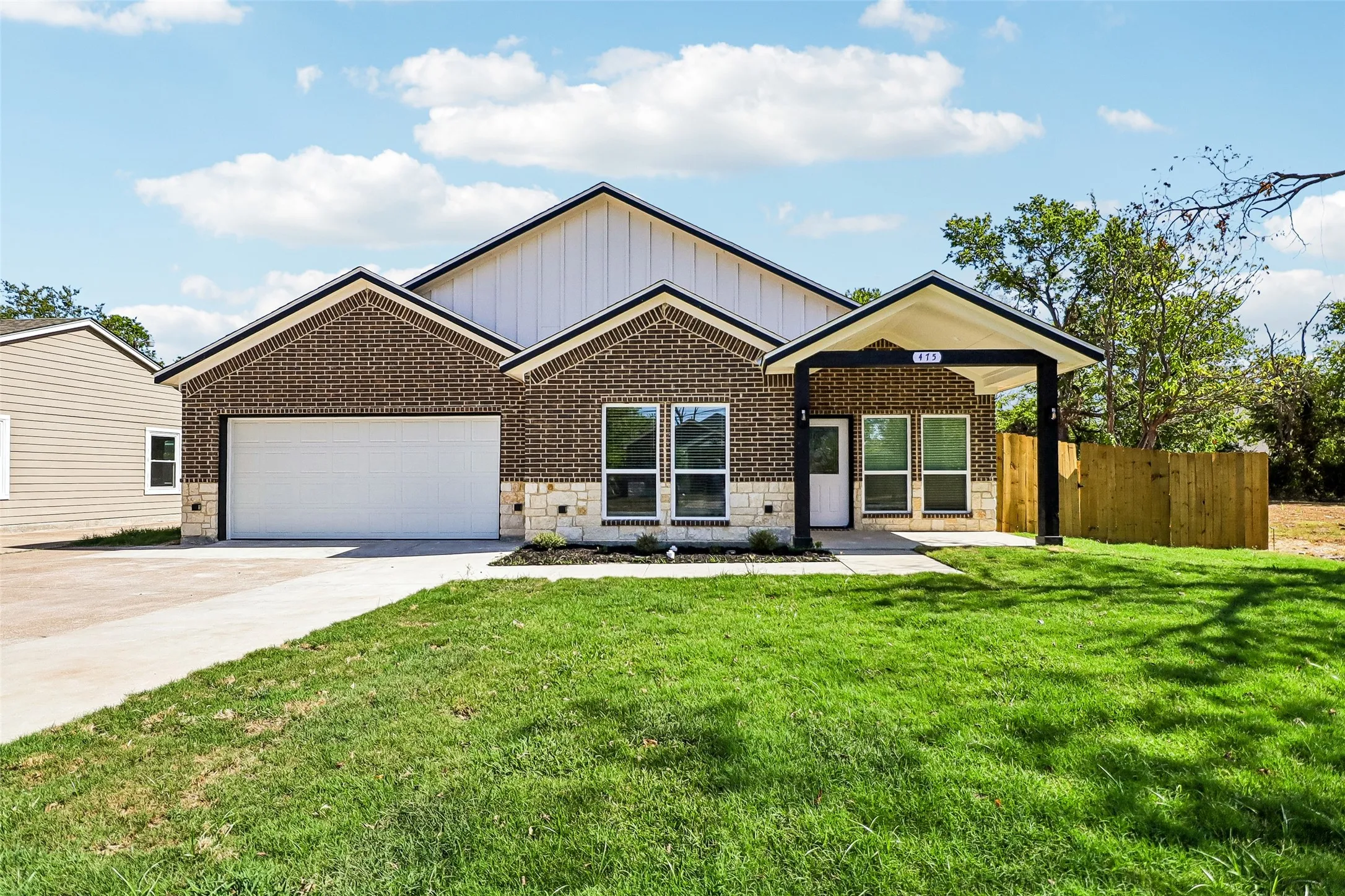 Brick and stone exterior with a covered entry, attached garage, concrete driveway, and manicured lawn