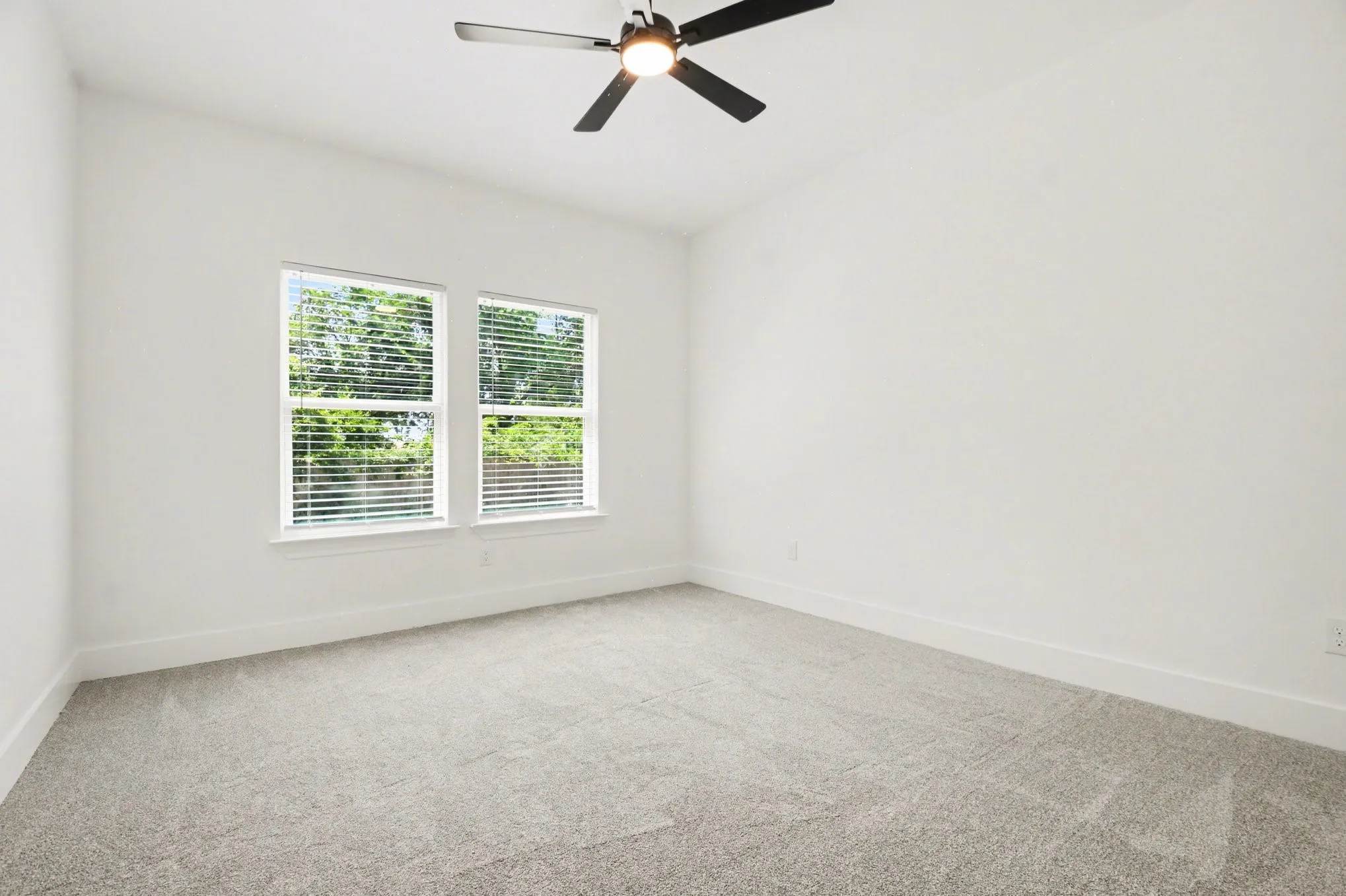 Carpeted room with white walls, two windows featuring blinds, and a ceiling fan with integrated lighting