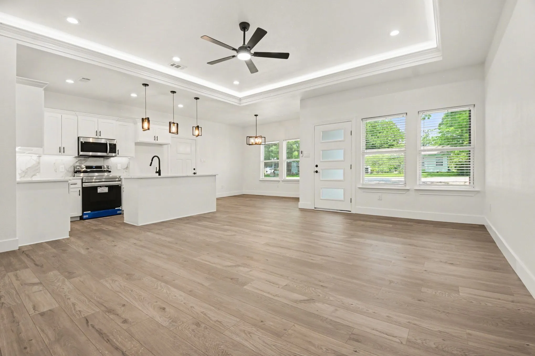 Wood-finish flooring throughout, white shaker cabinetry, stainless steel appliances, tray ceiling with recessed lighting, and modern pendant light fixtures