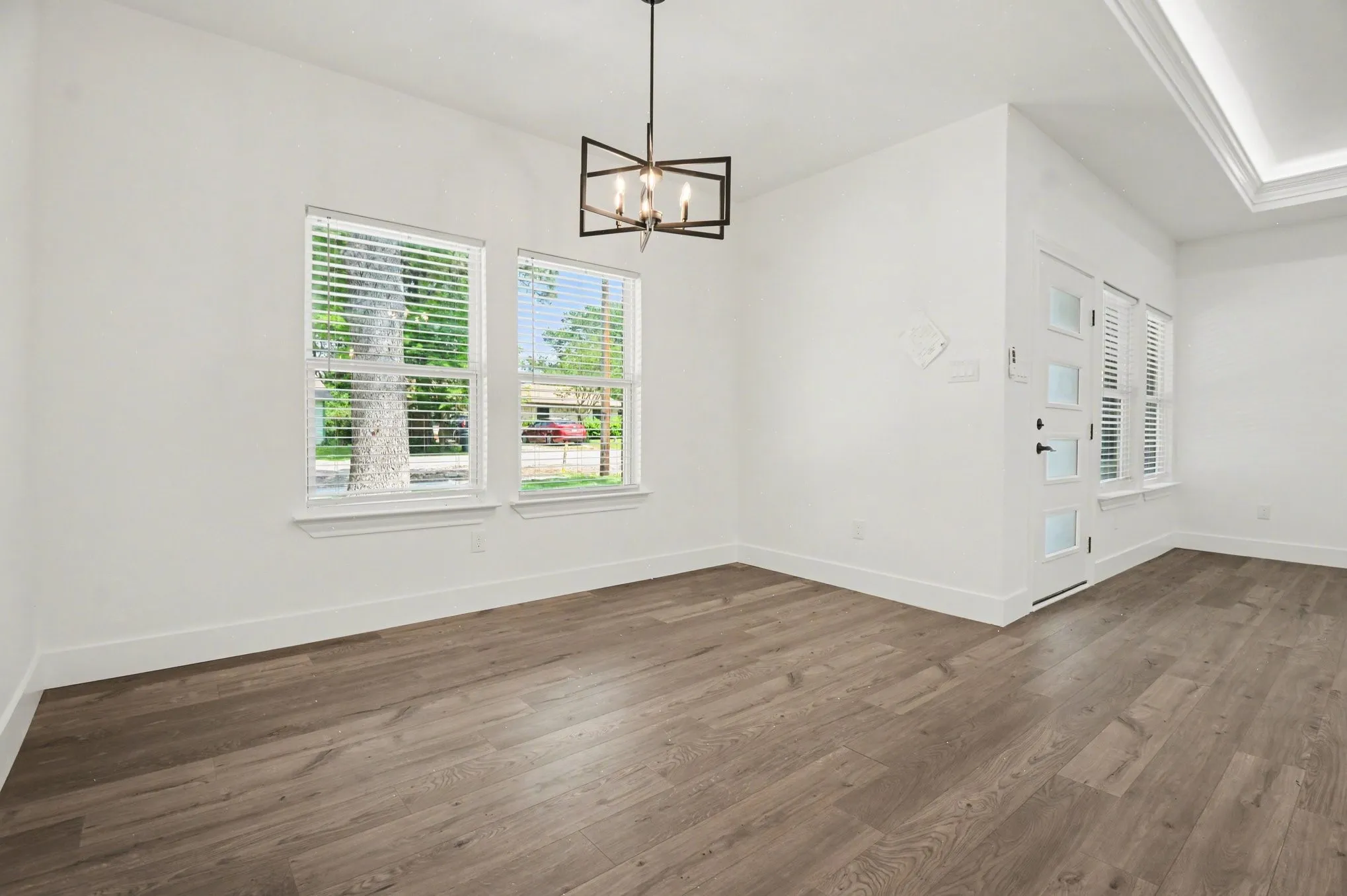 Wood-finish flooring, white walls, two windows with blinds, a modern chandelier, and a white entry door with frosted glass panels