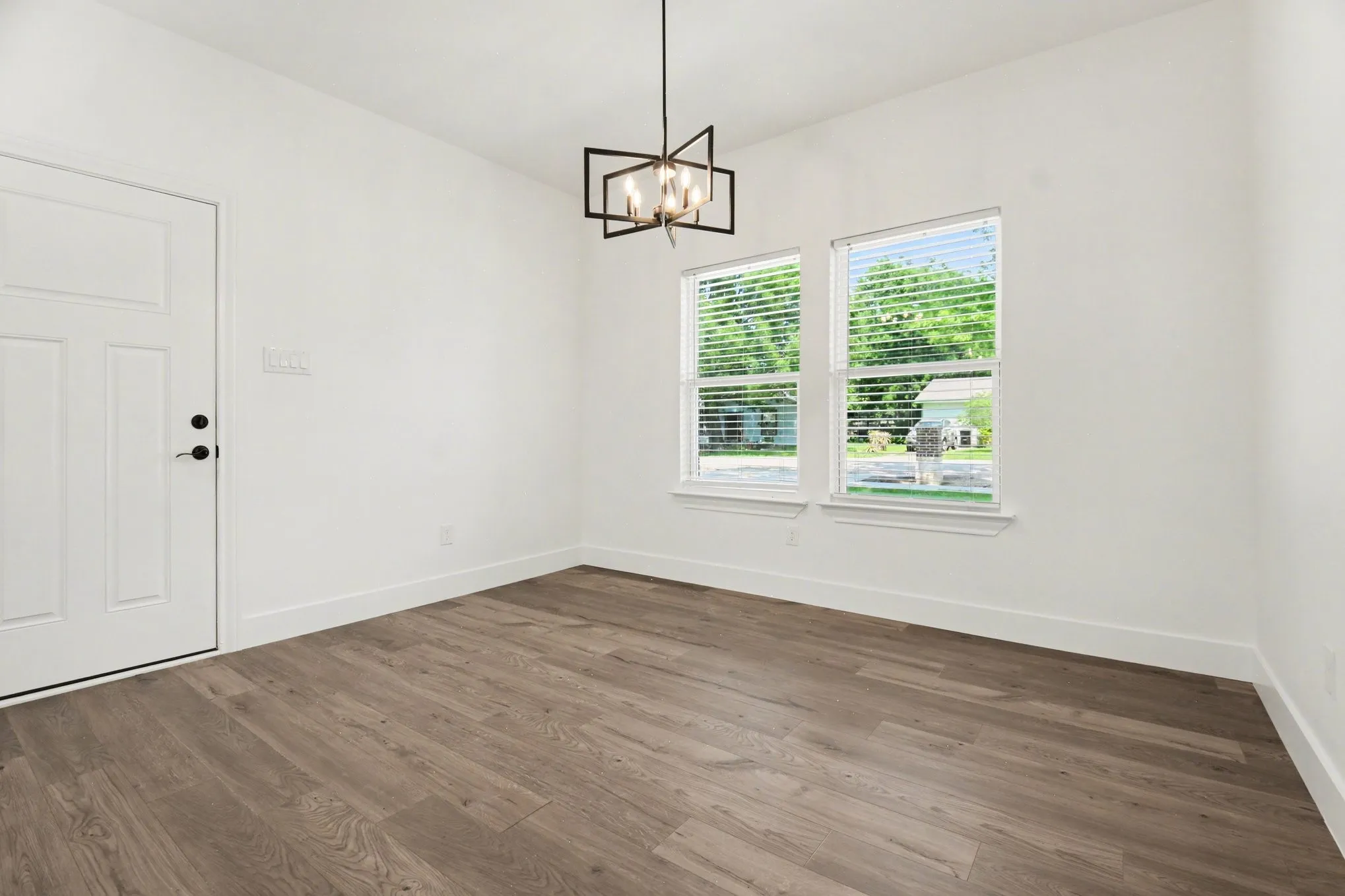 Wood-finish flooring, white walls, two windows with blinds, and a modern geometric light fixture