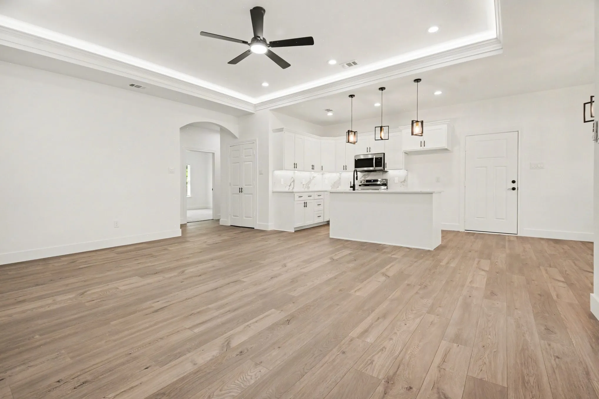 Wood-finish flooring throughout, white shaker cabinetry with dark hardware, recessed lighting, white countertops and backsplash, and a modern ceiling fan