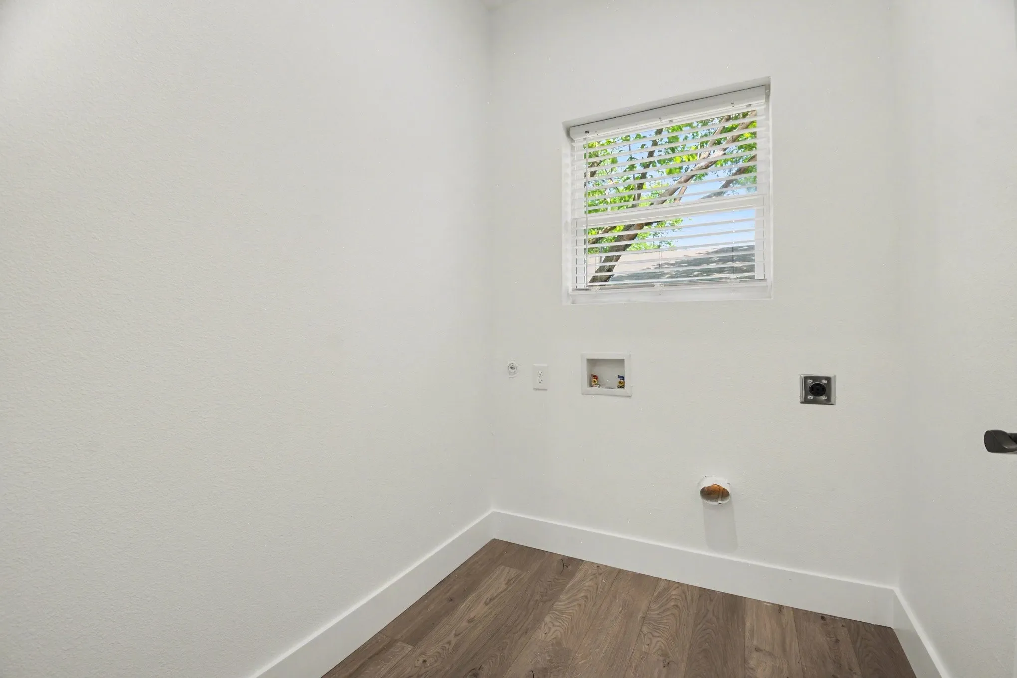 Bright utility room with large transom window providing natural light, wood-finish flooring, fresh white walls, and multiple electrical outlets for convenient functionality