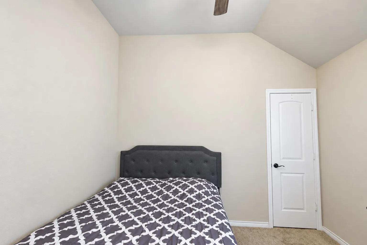 Neutral-toned walls, vaulted ceiling, white paneled door with black hardware, and carpeted flooring