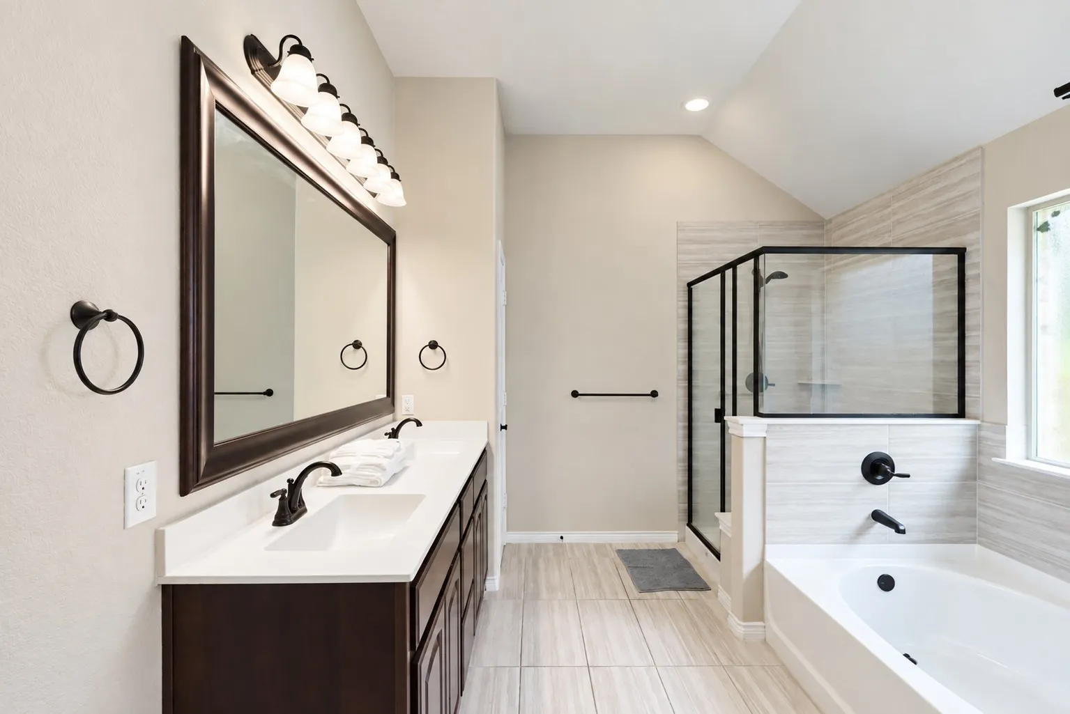 Dual vanity with white countertops, dark wood-finish cabinetry, and framed mirror