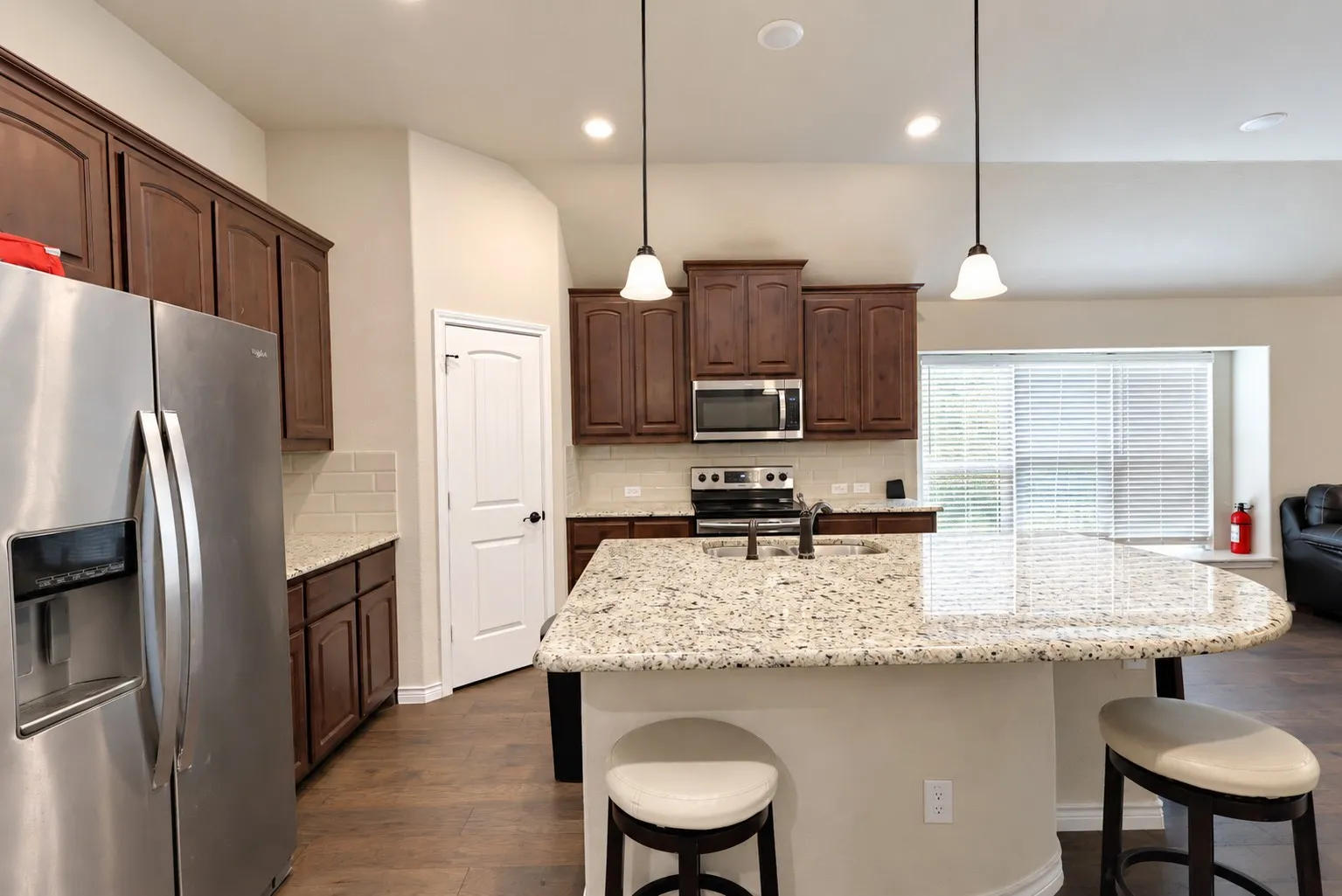 Spacious kitchen featuring dark wood cabinetry, a large kitchen island with a light-colored countertop, stainless steel appliances, and wood-finish flooring