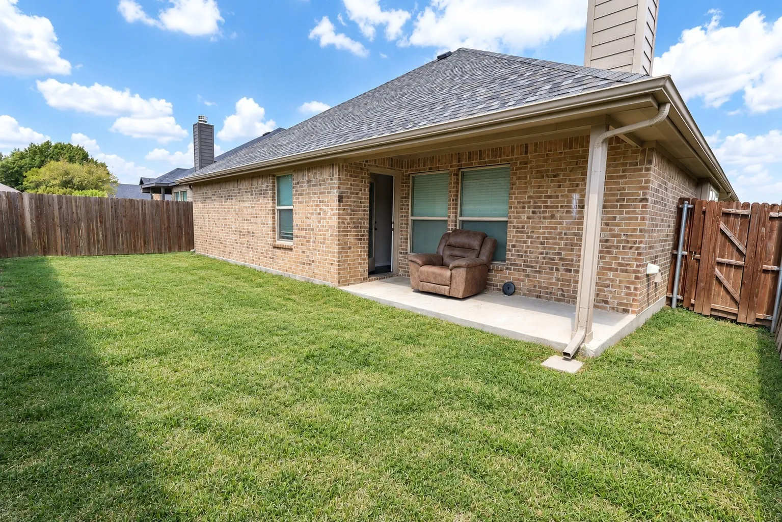 Private backyard with a covered concrete patio, brick exterior, and wood fencing