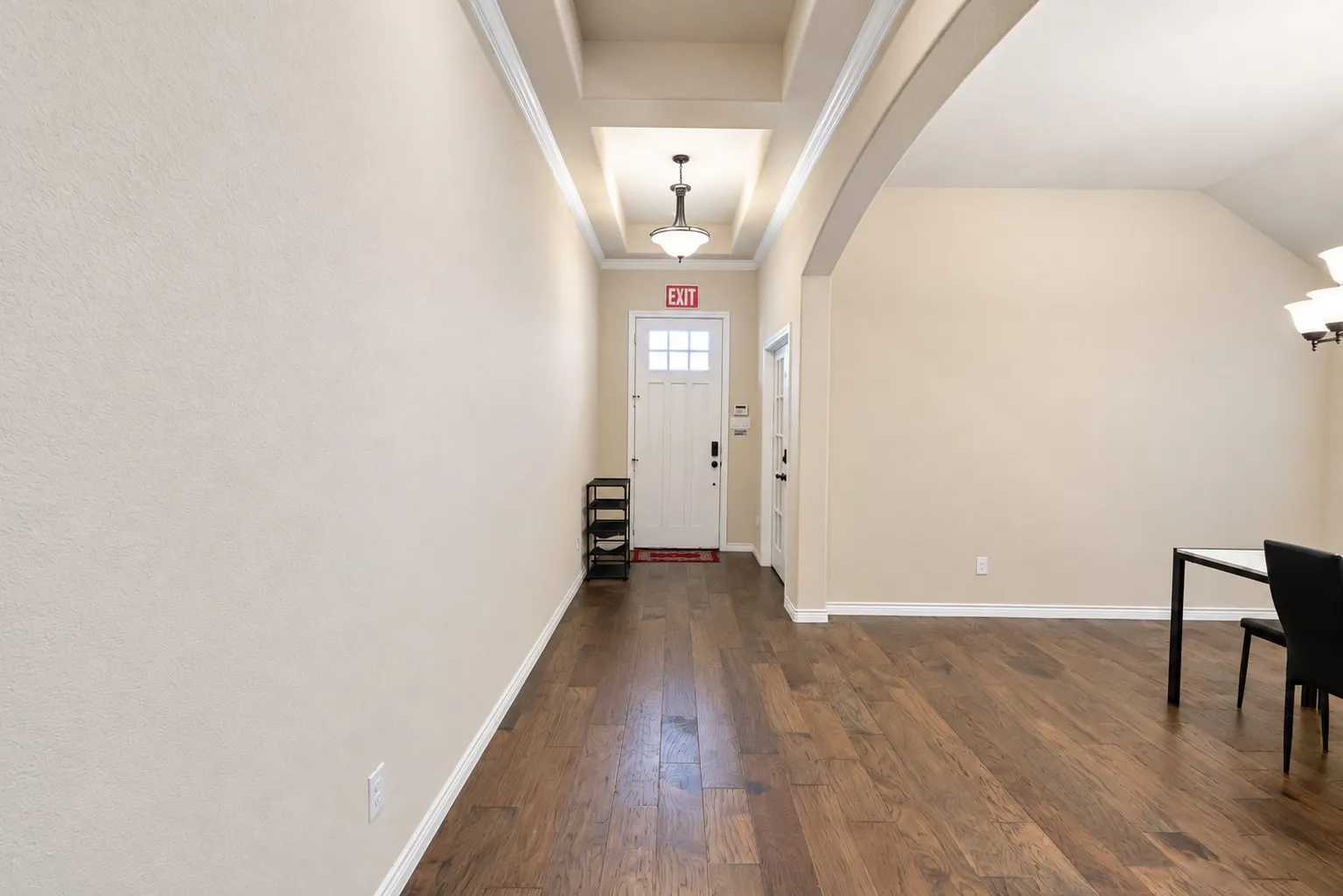 Wood-finish flooring throughout, tray ceiling with recessed lighting, arched doorway, and solid panel door with frosted glass inserts