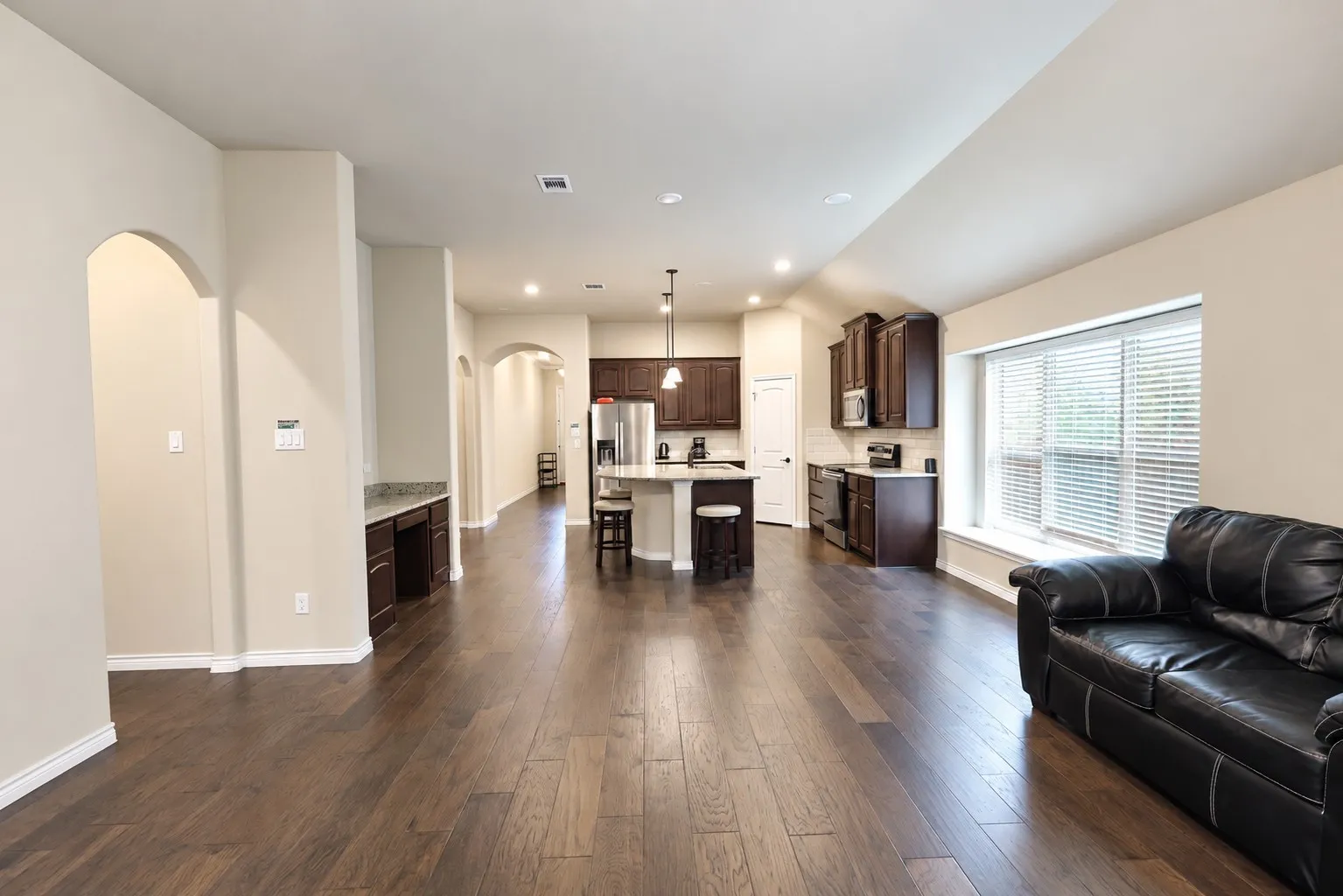 Open-concept living space with wood-finish flooring, a kitchen island, recessed lighting, and a built-in desk area