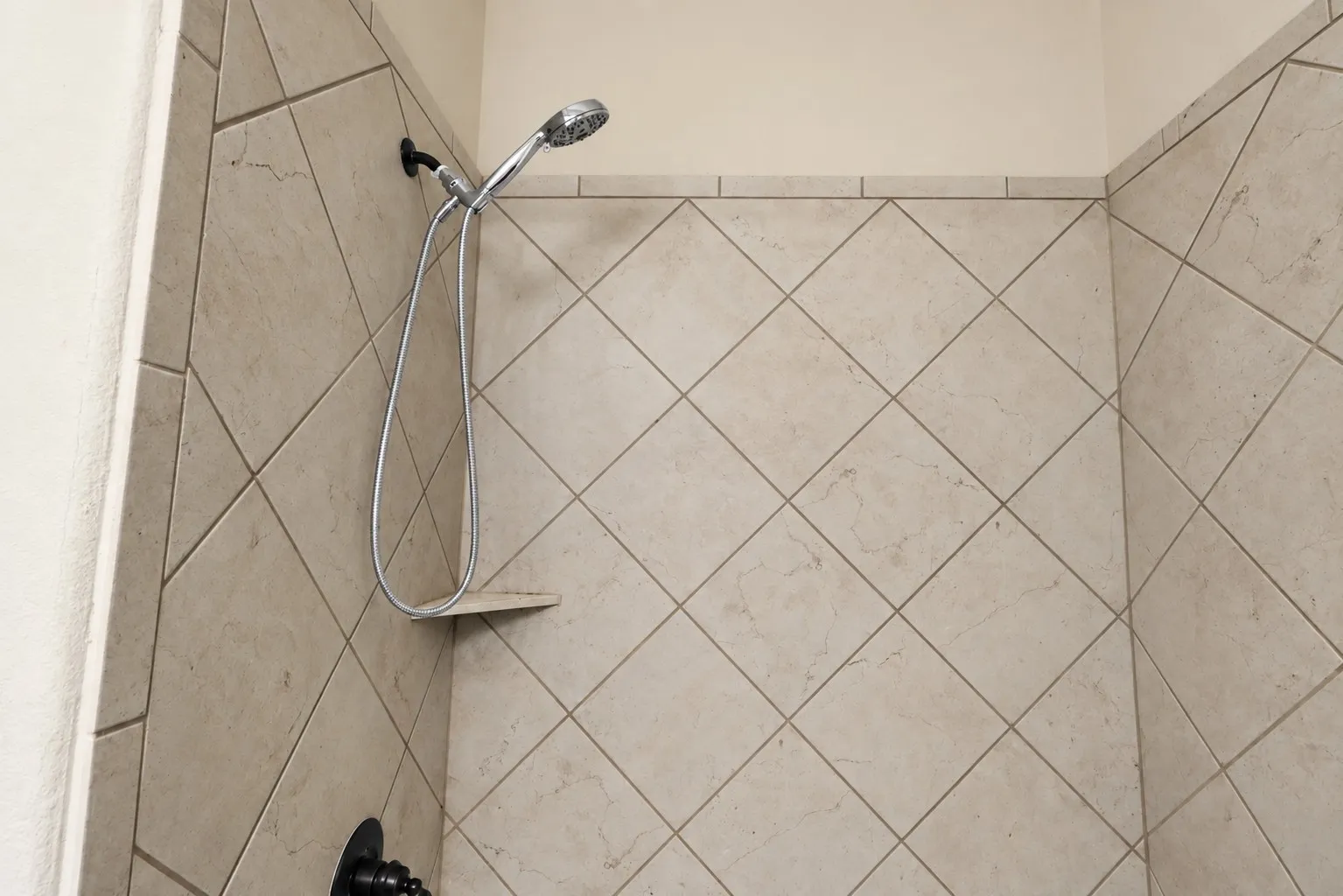 Tiled shower enclosure featuring a handheld showerhead and built-in corner shelf