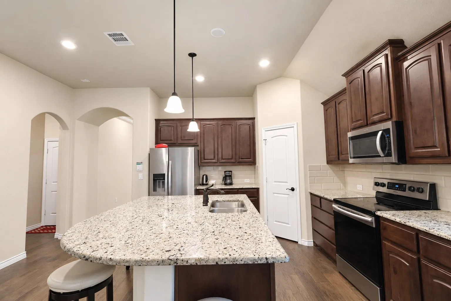 Kitchen featuring a large island, wood-finish flooring, recessed lighting, pendant lights, and stainless steel appliances