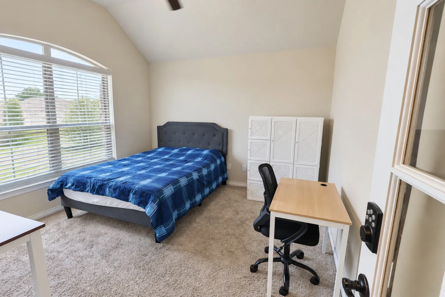 Vaulted ceiling, arched window with blinds, neutral-toned carpeting, and a ceiling fan