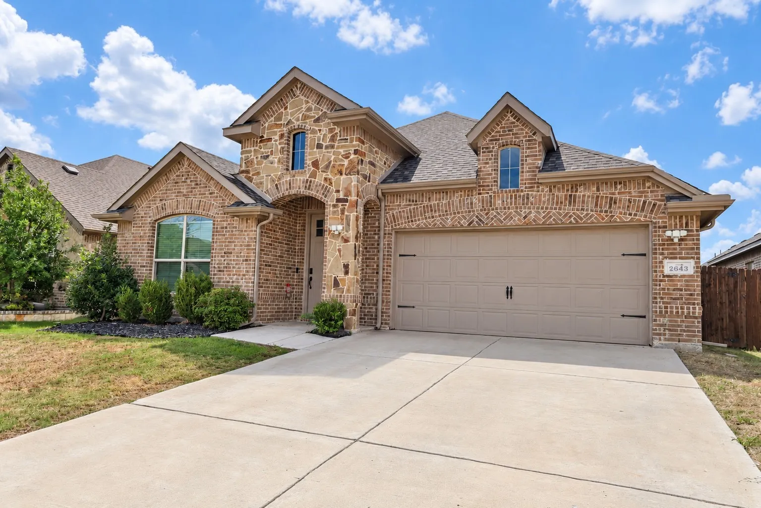 Brick and stone exterior with a neutral garage door, concrete driveway, and front landscaping