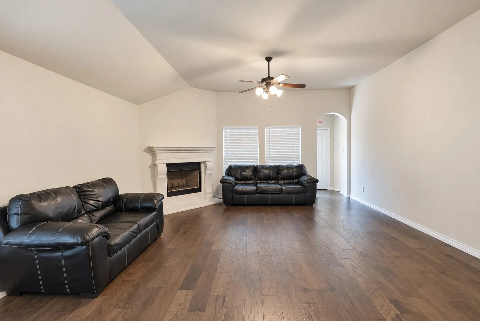 Spacious living area featuring wood-finish flooring, a corner fireplace with a decorative mantel, vaulted ceilings, and a ceiling fan with integrated lighting