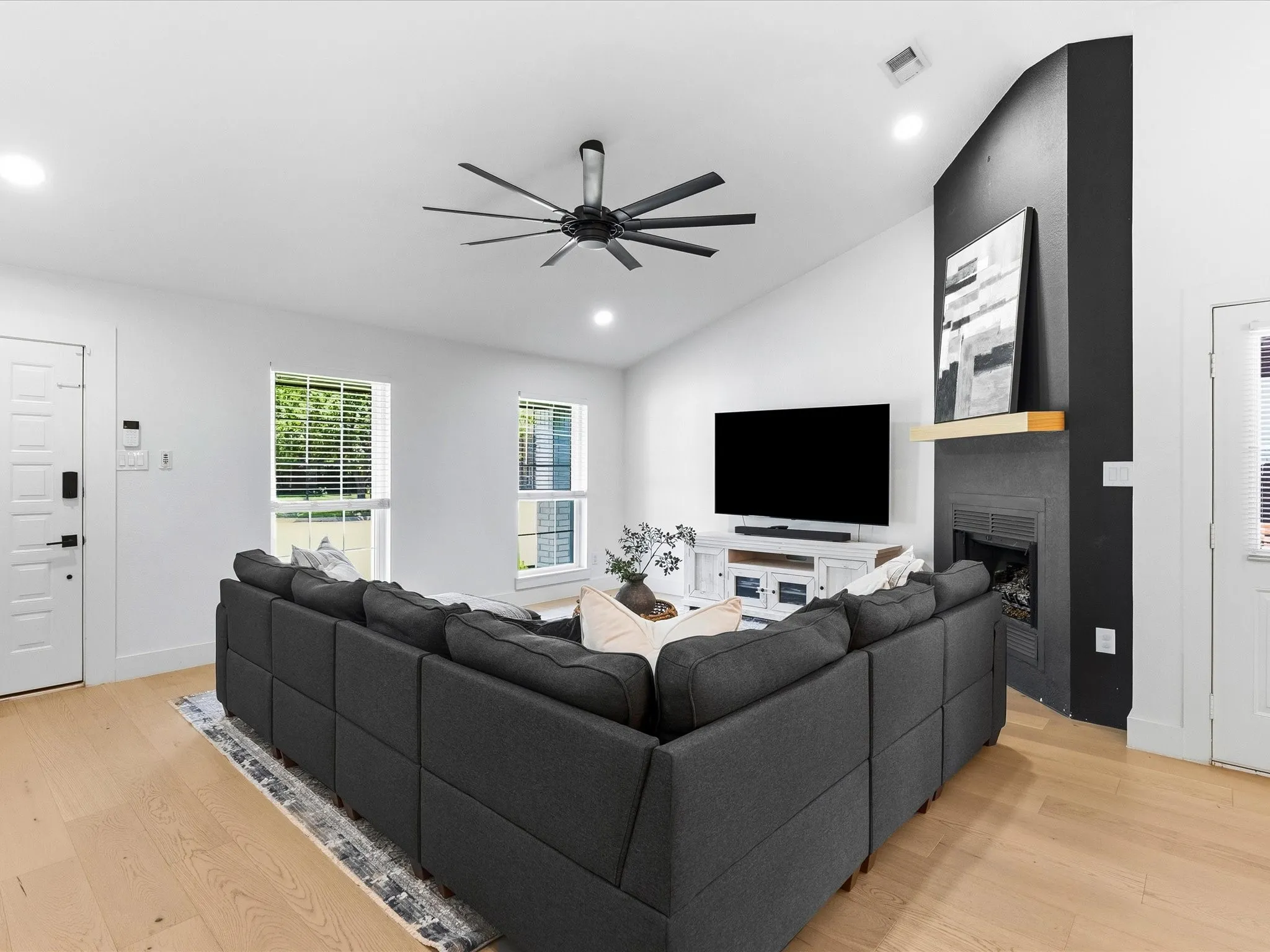 Vaulted ceiling with a contemporary ceiling fan, light wood-finish flooring, and a fireplace featuring a dark surround and light wood mantel