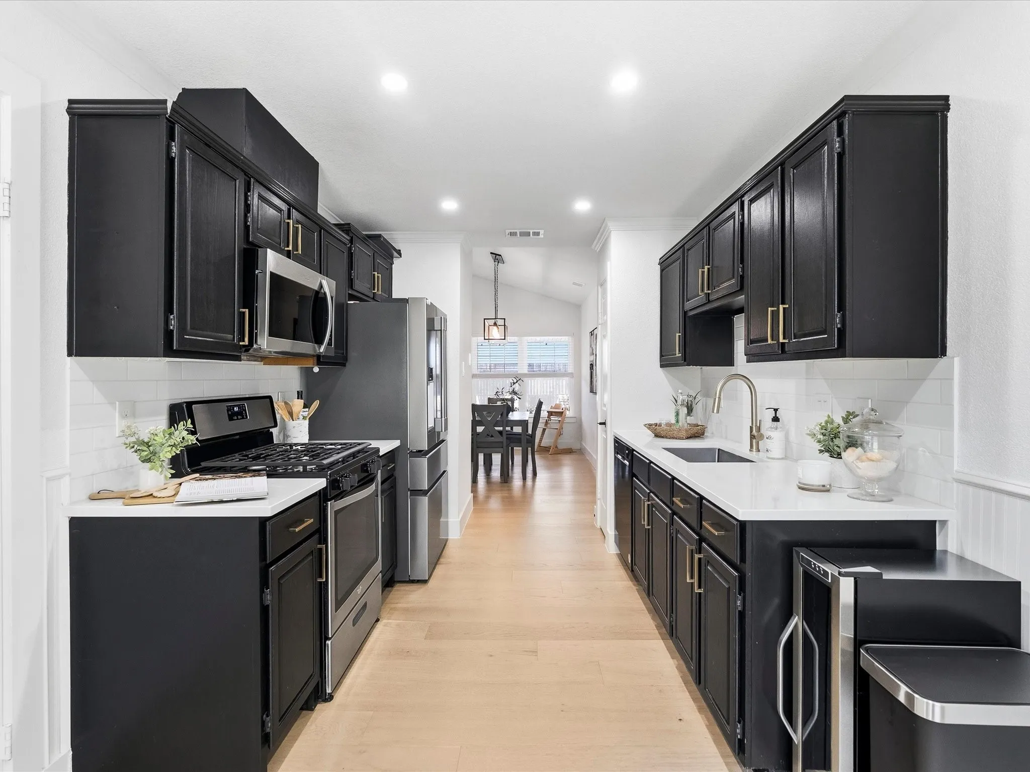 Galley kitchen featuring black cabinetry, white countertops, stainless steel appliances, a subway tile backsplash, and light wood-finish flooring