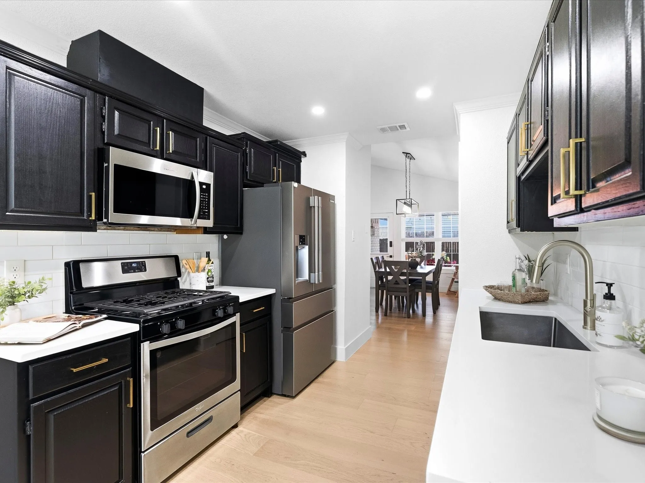 Kitchen featuring black cabinetry, stainless steel appliances, white subway tile backsplash, light wood-finish flooring, and white countertops