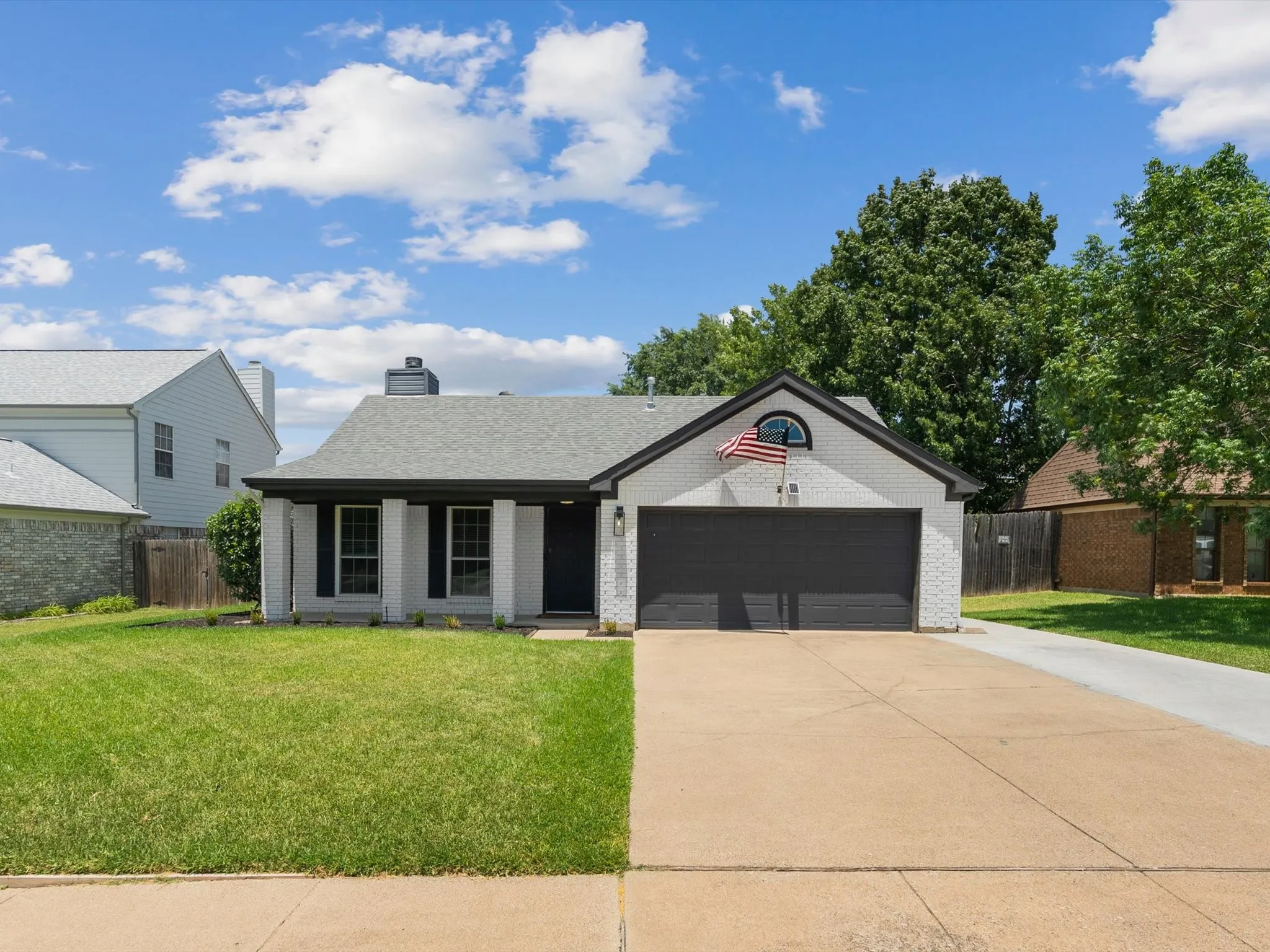 White brick exterior with a dark-trimmed gable, a two-car garage, and a covered entry with columns