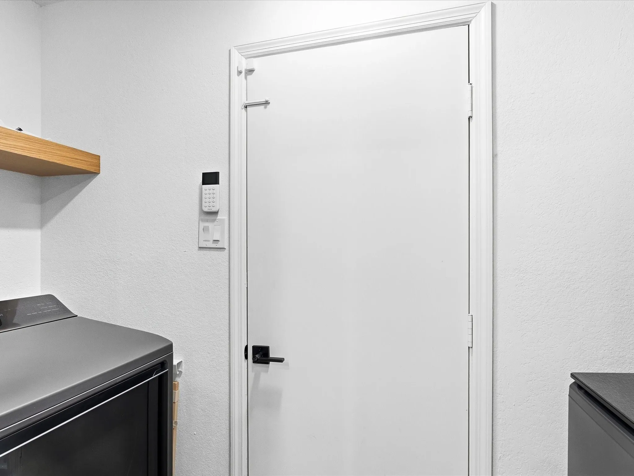 White interior door with a black lever handle, white trim, and a floating wood-finish shelf