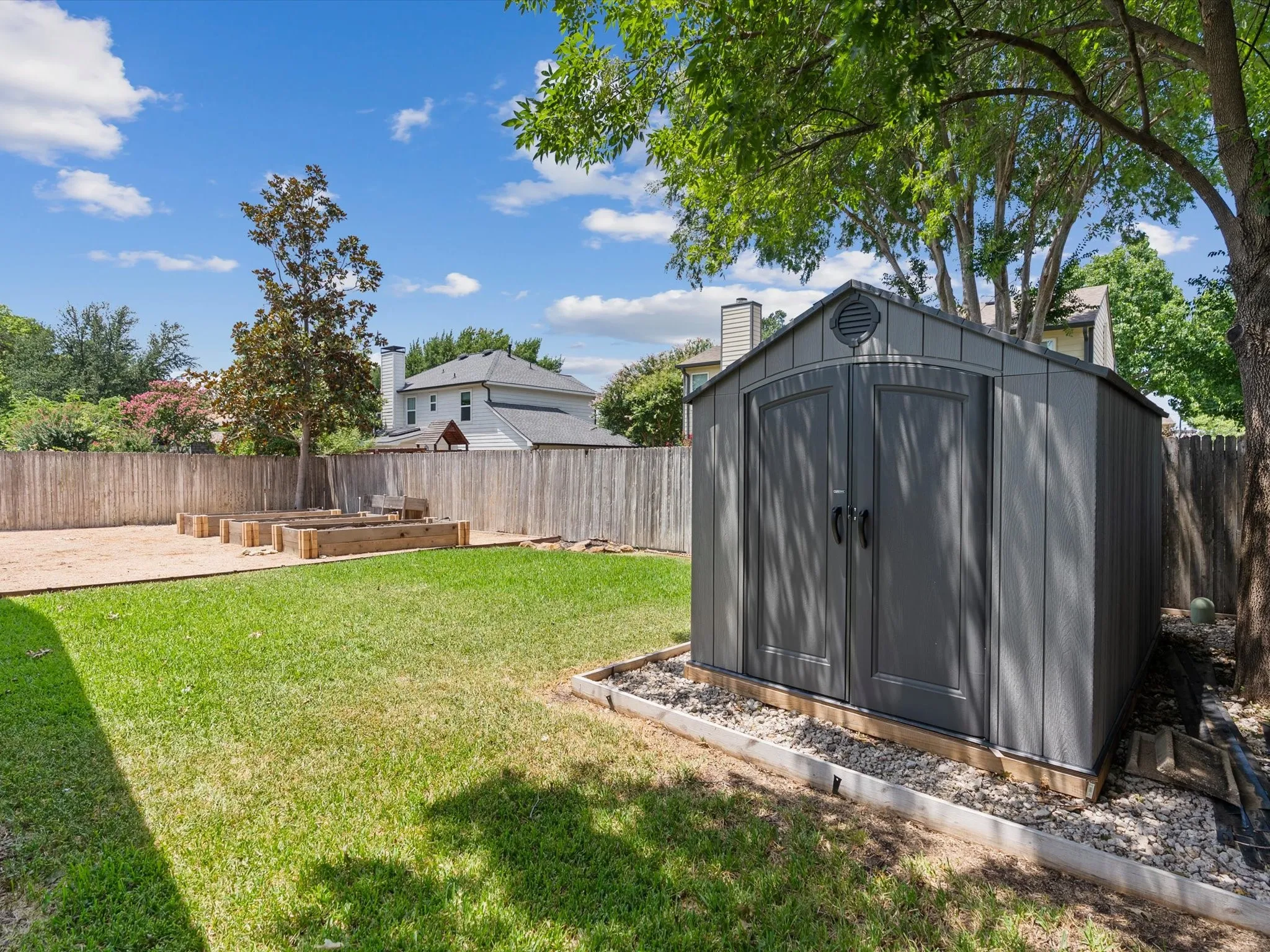 Expansive backyard with a manicured lawn, a detached storage shed, and raised garden beds