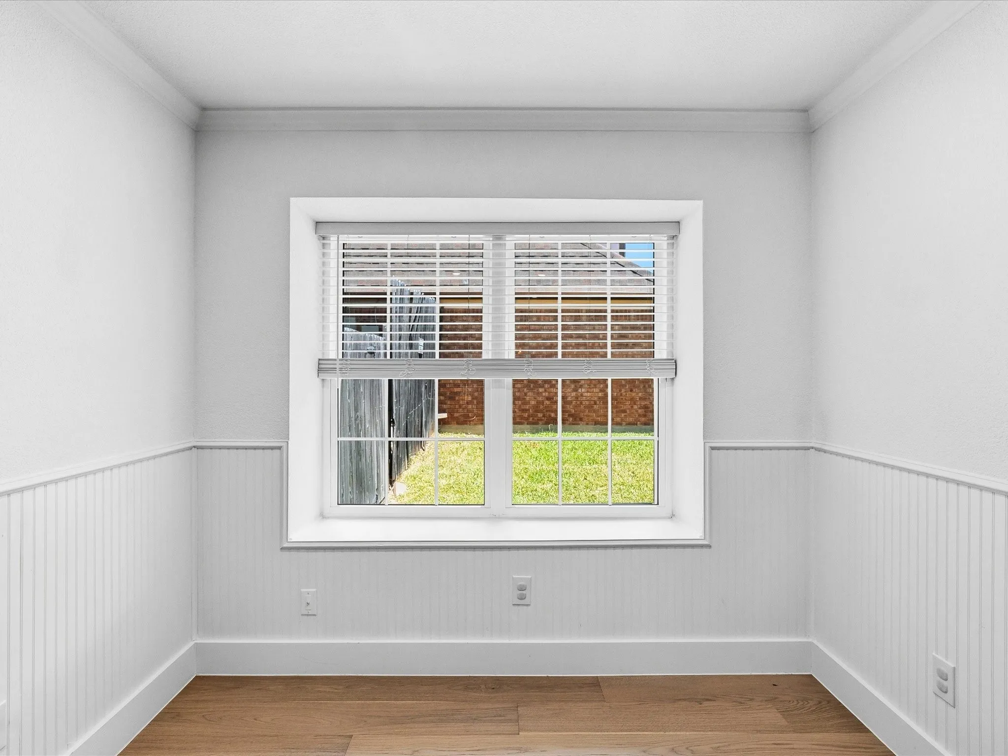 Wood-finish flooring, white beadboard wainscoting, crown molding, and a double-pane window with horizontal blinds