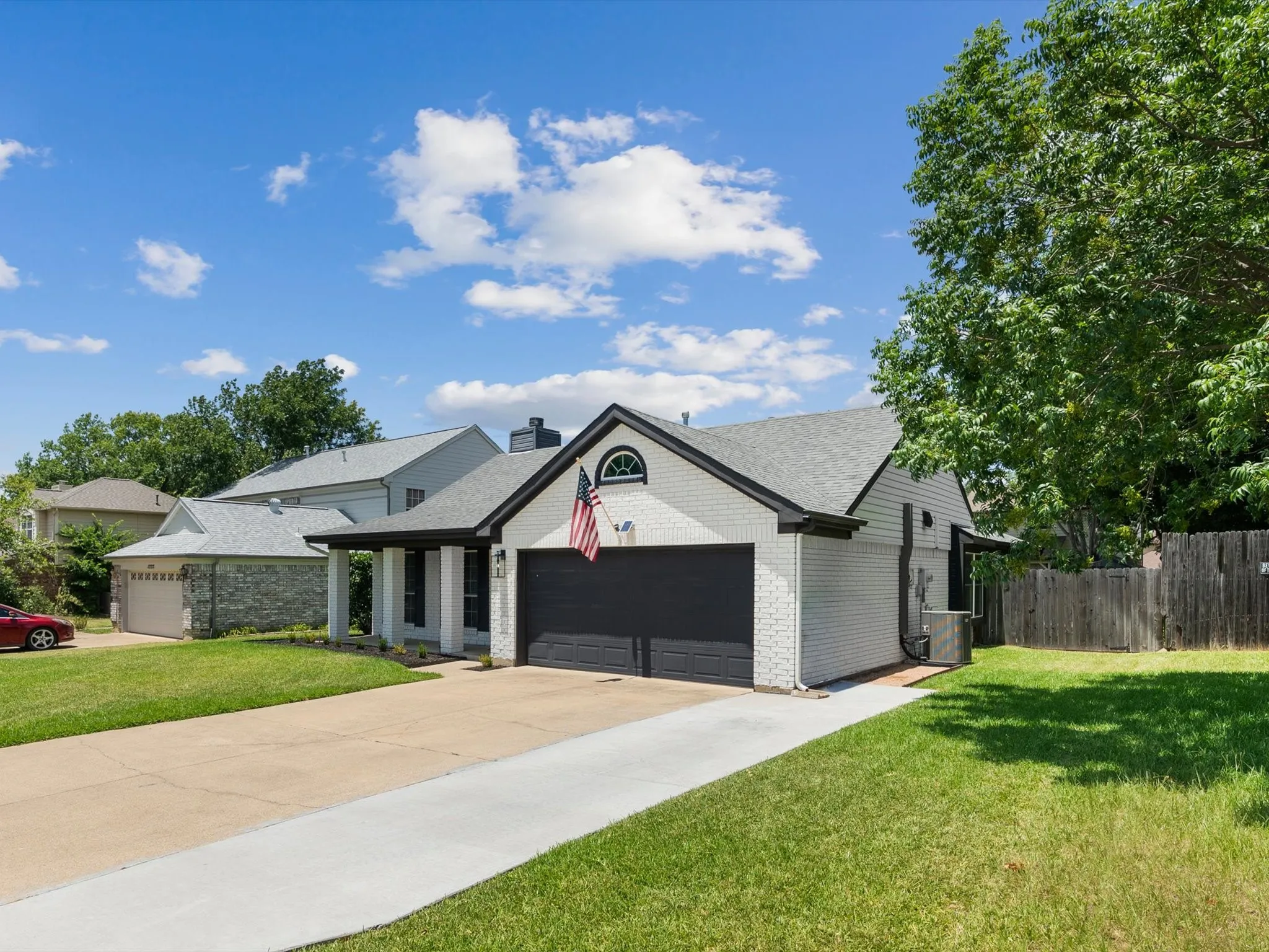 White brick exterior with dark trim accents, attached garage with dark door, arched window detail, and covered entry