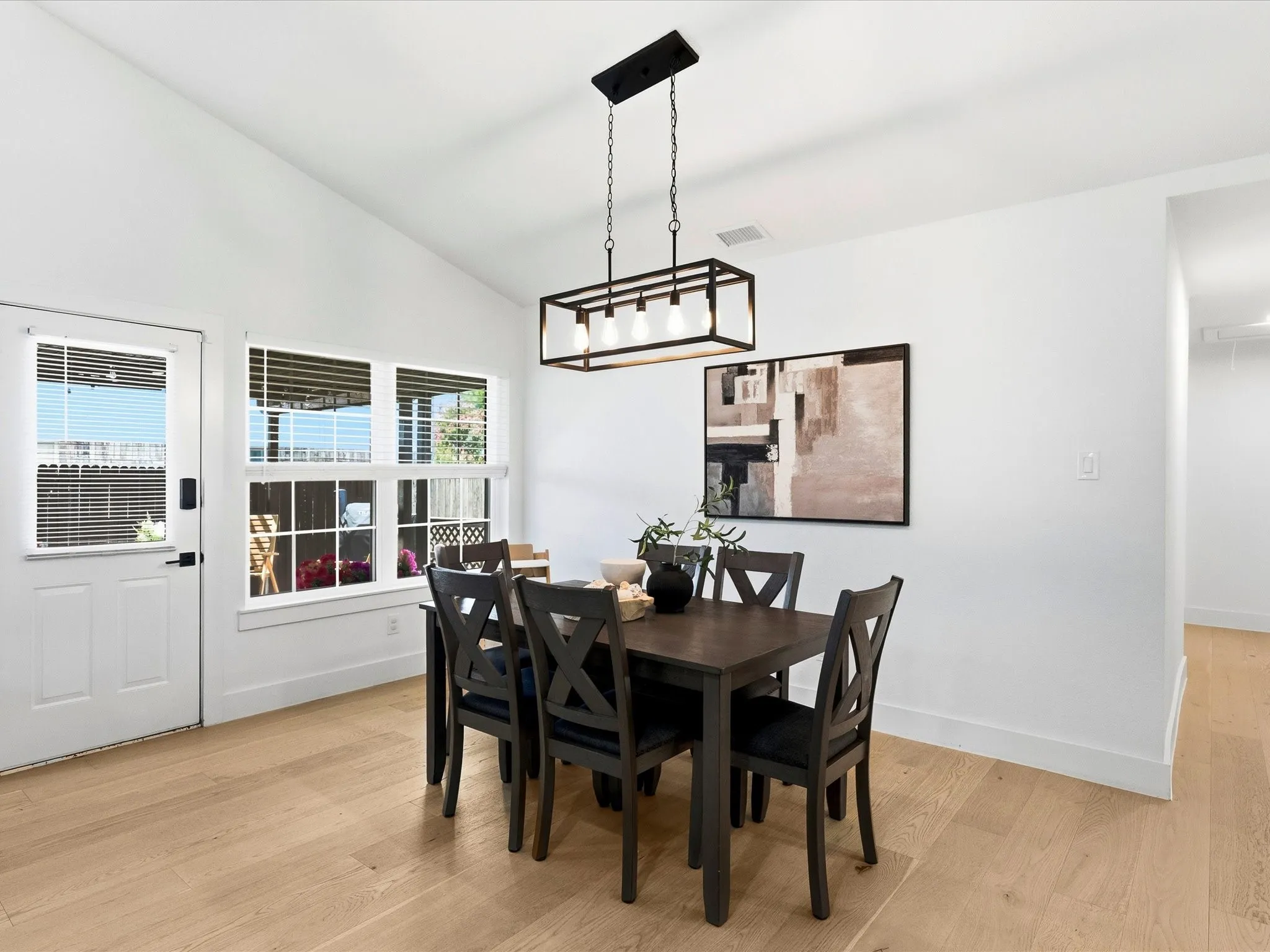 Vaulted ceiling, light wood-finish flooring, white walls, multiple windows, and a black linear chandelier