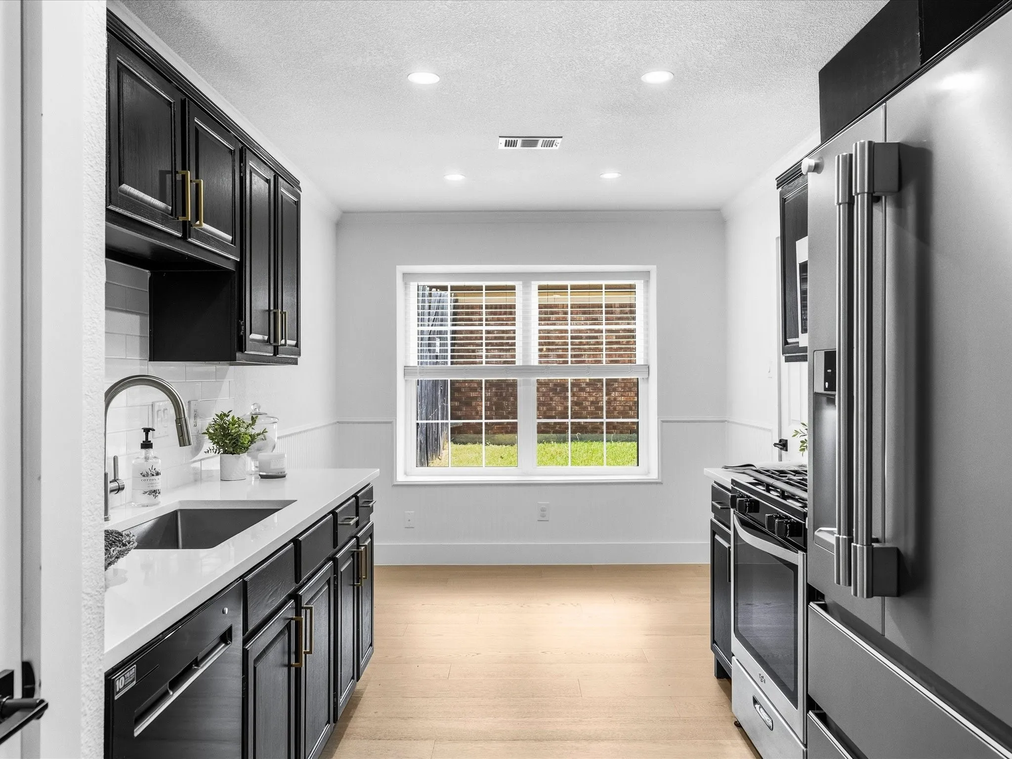 Kitchen featuring black cabinetry with gold-finish hardware, stainless steel appliances, a stainless steel sink with a gooseneck faucet, light-toned flooring, and recessed lighting