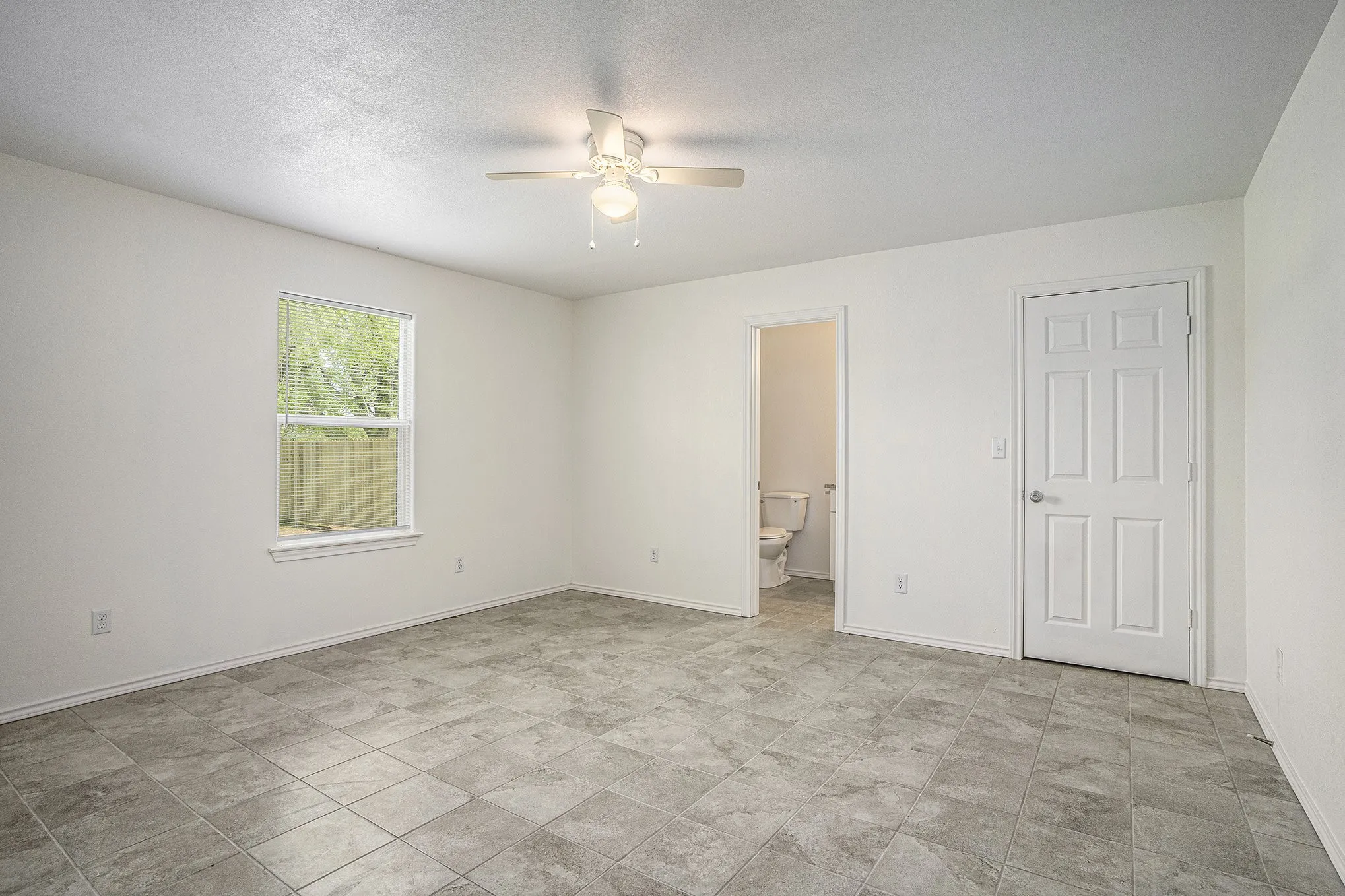 Spacious room with square tile flooring, a ceiling fan with integrated lighting, and a window providing natural light