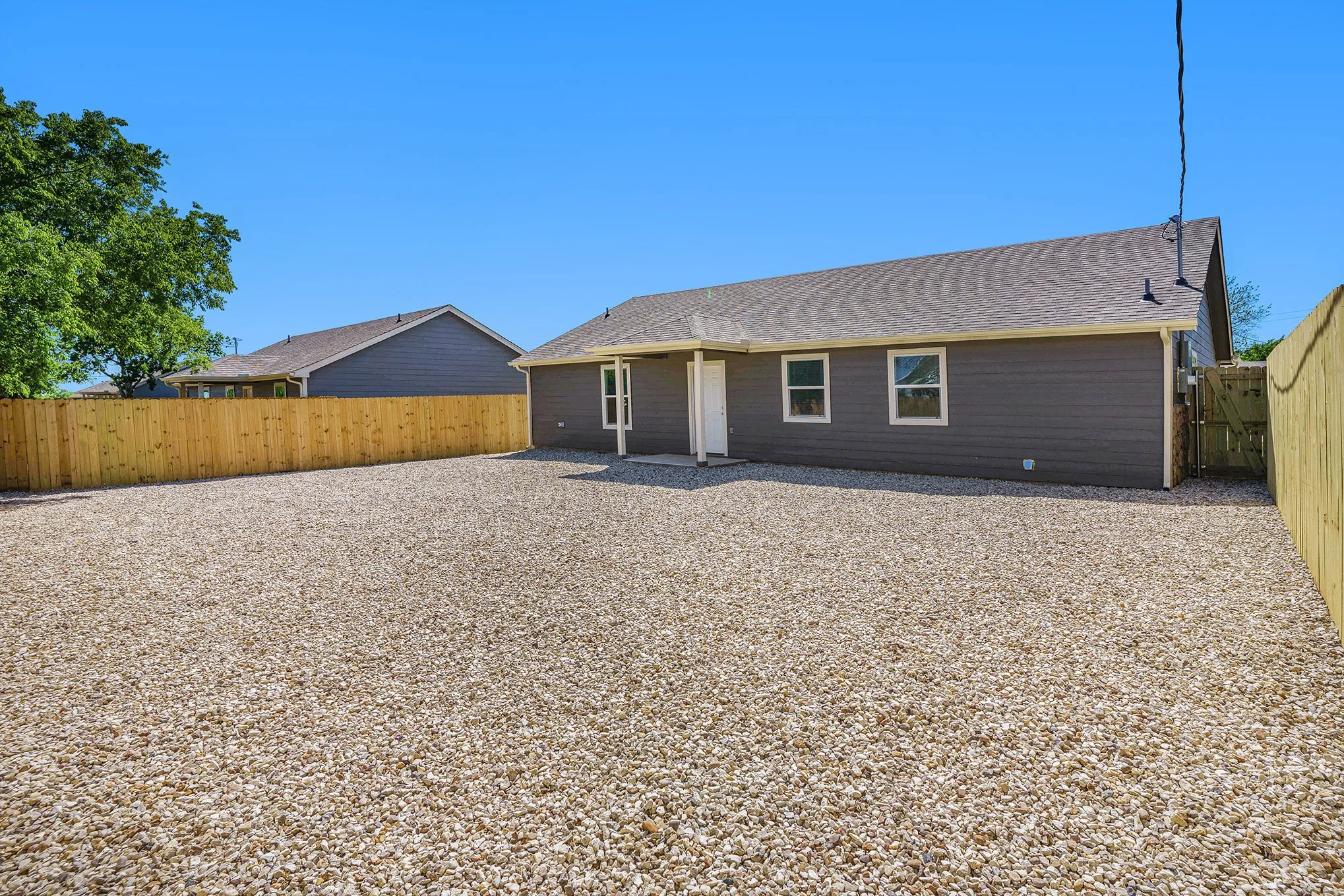 Gravel patio area featuring a privacy fence and exterior lighting