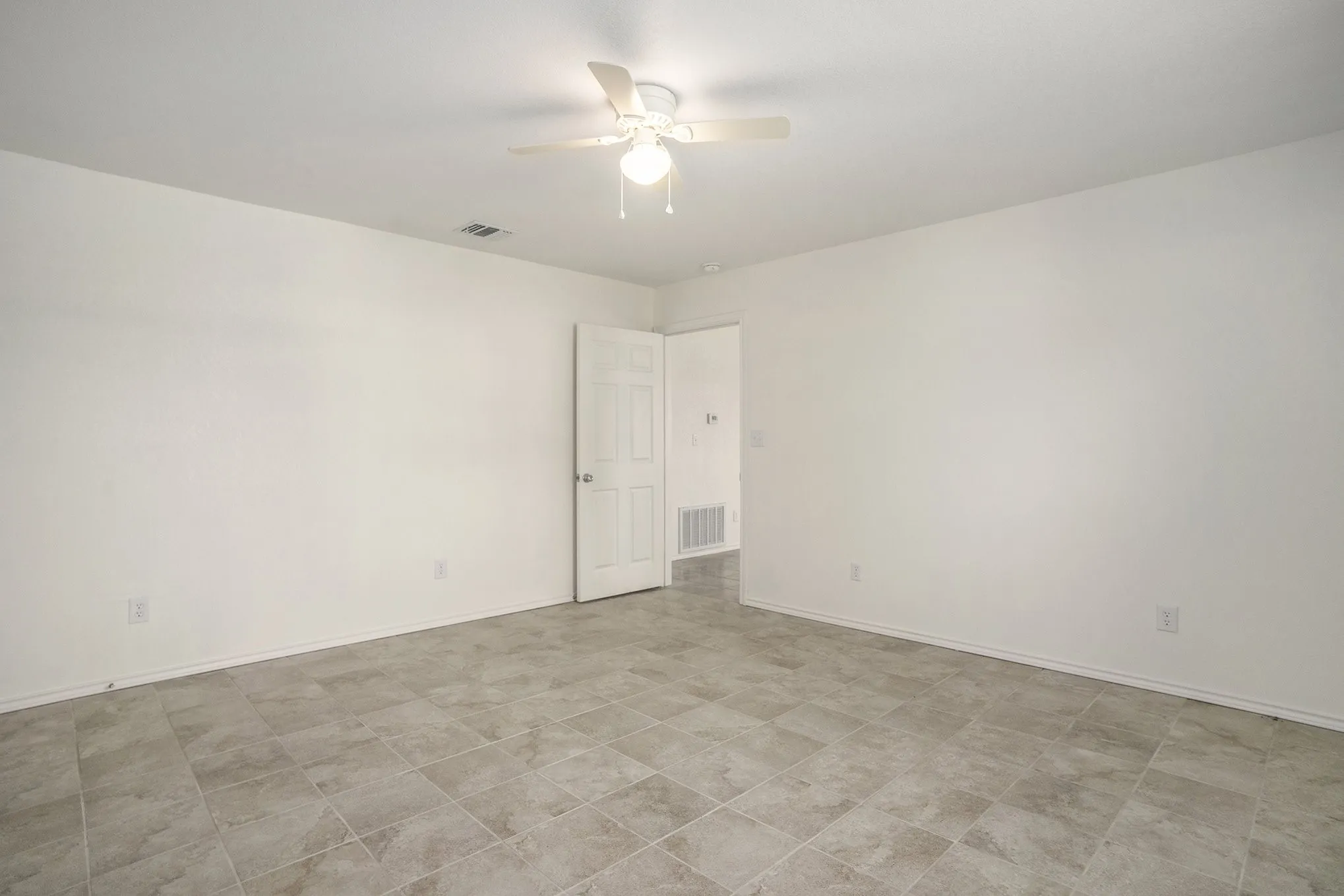Spacious room with light-colored tile flooring, white walls, and a ceiling fan with integrated lighting