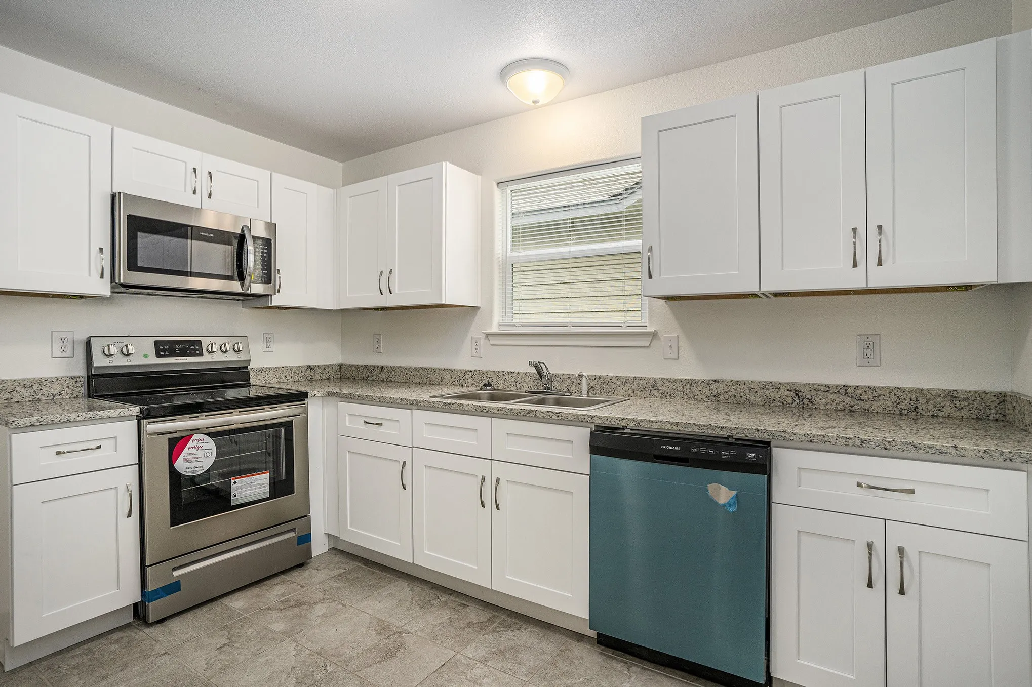 Modern kitchen featuring stainless steel appliances, white cabinetry, a double basin sink, and stone-finish countertops