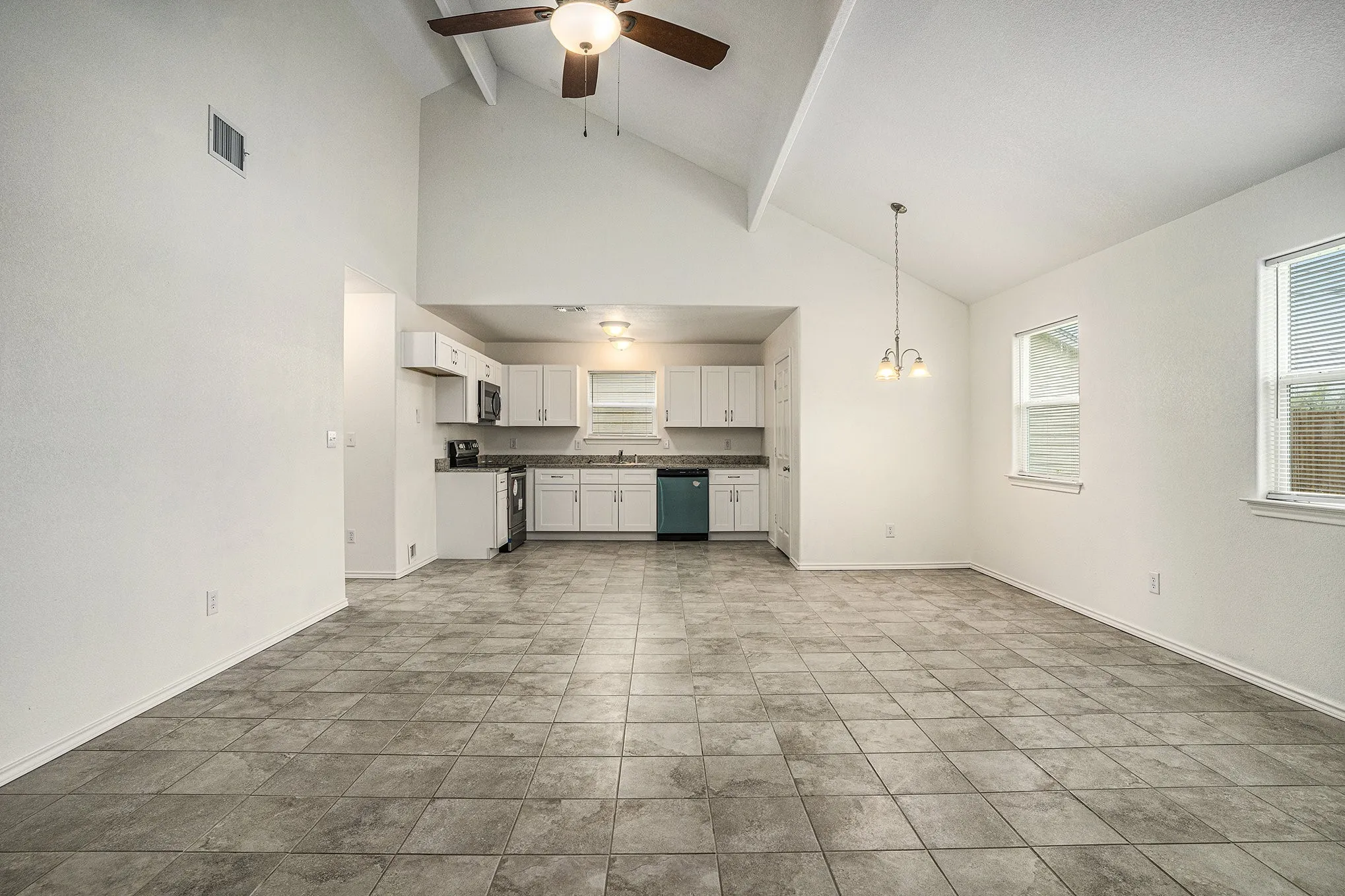 Vaulted ceiling, ceiling fan, tile flooring, white cabinetry, and a built-in kitchen appliance suite