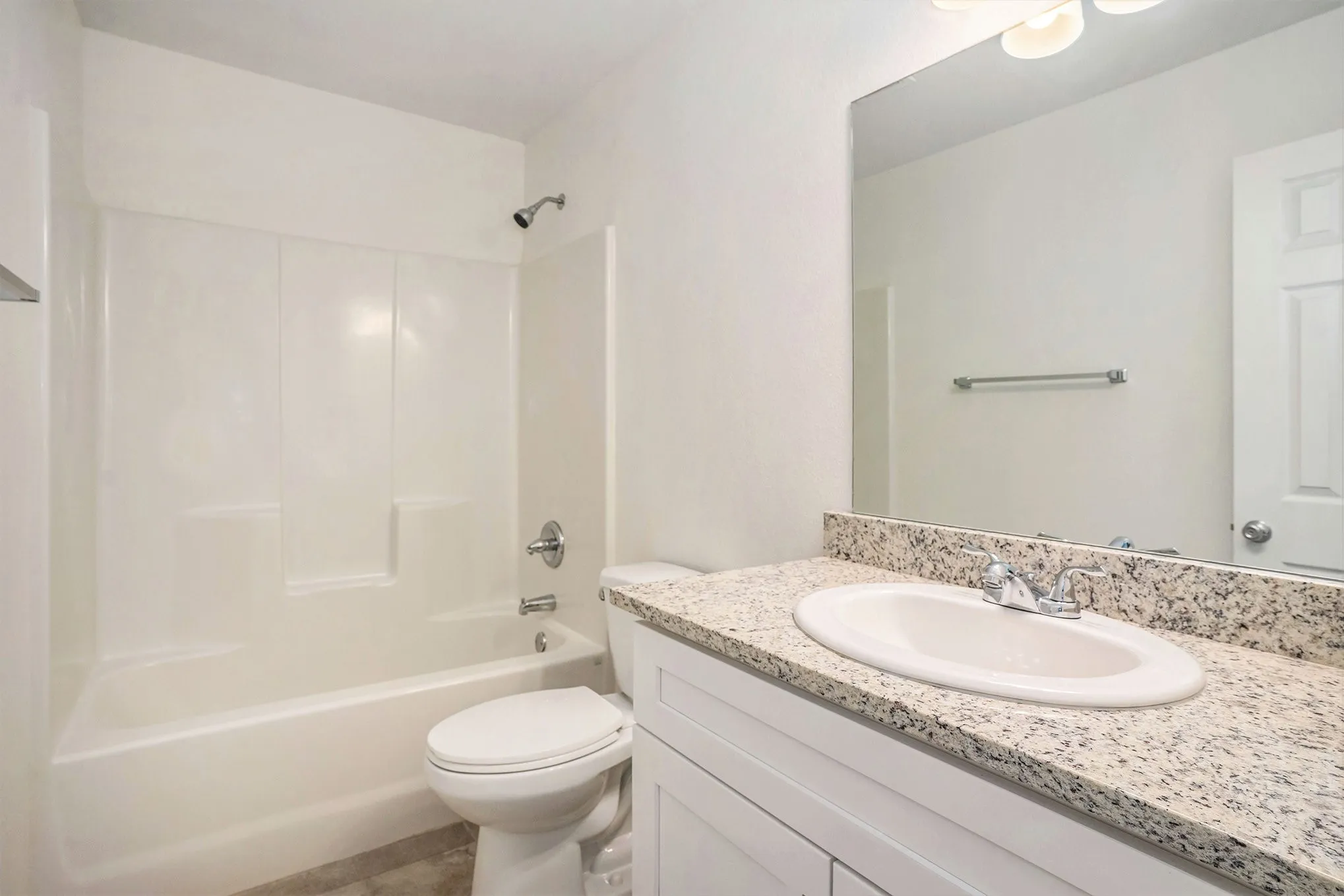 White vanity with a stone-finish countertop, integrated sink, and chrome fixtures