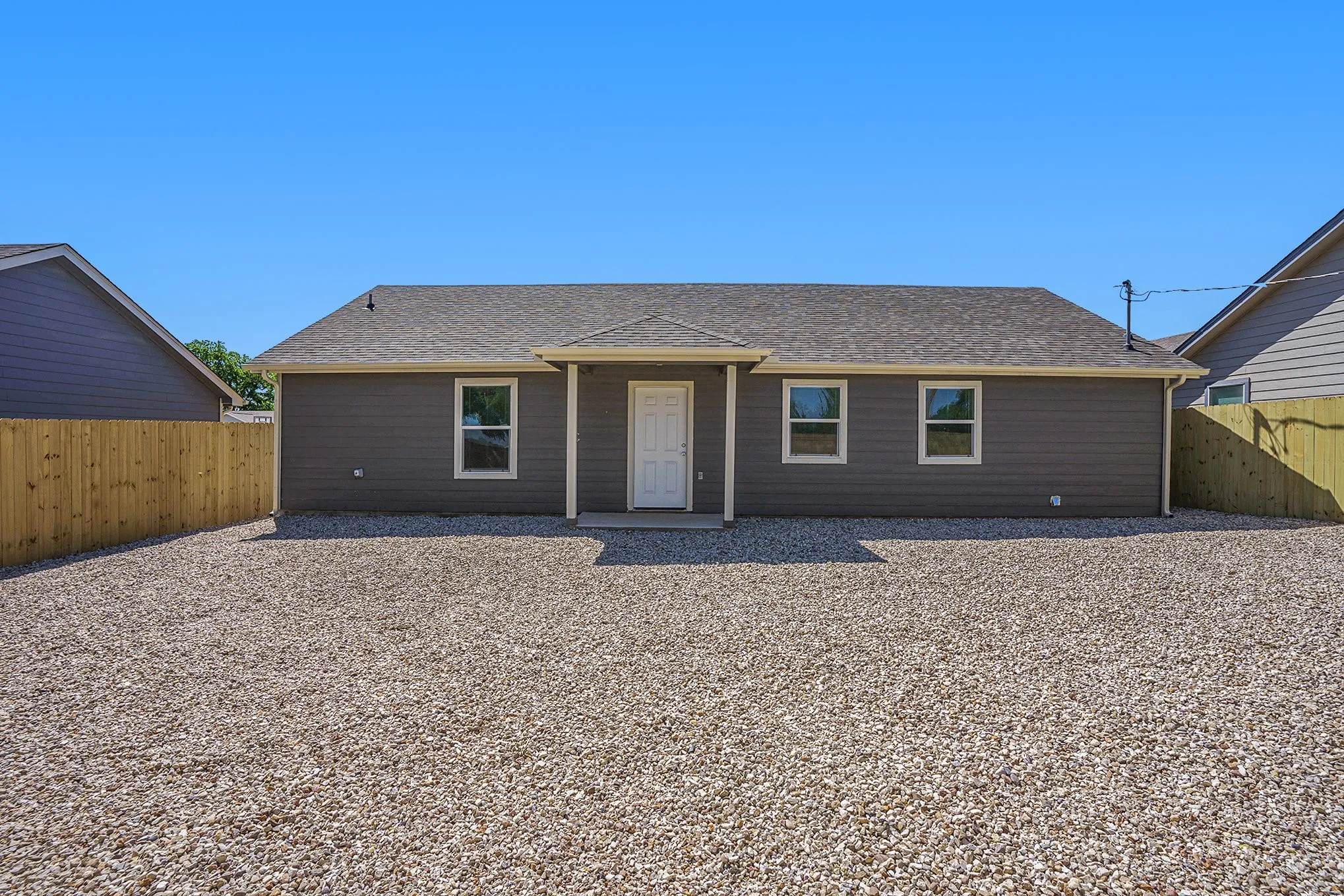 Single-story exterior with horizontal siding, a light gray roof, and a gravel yard