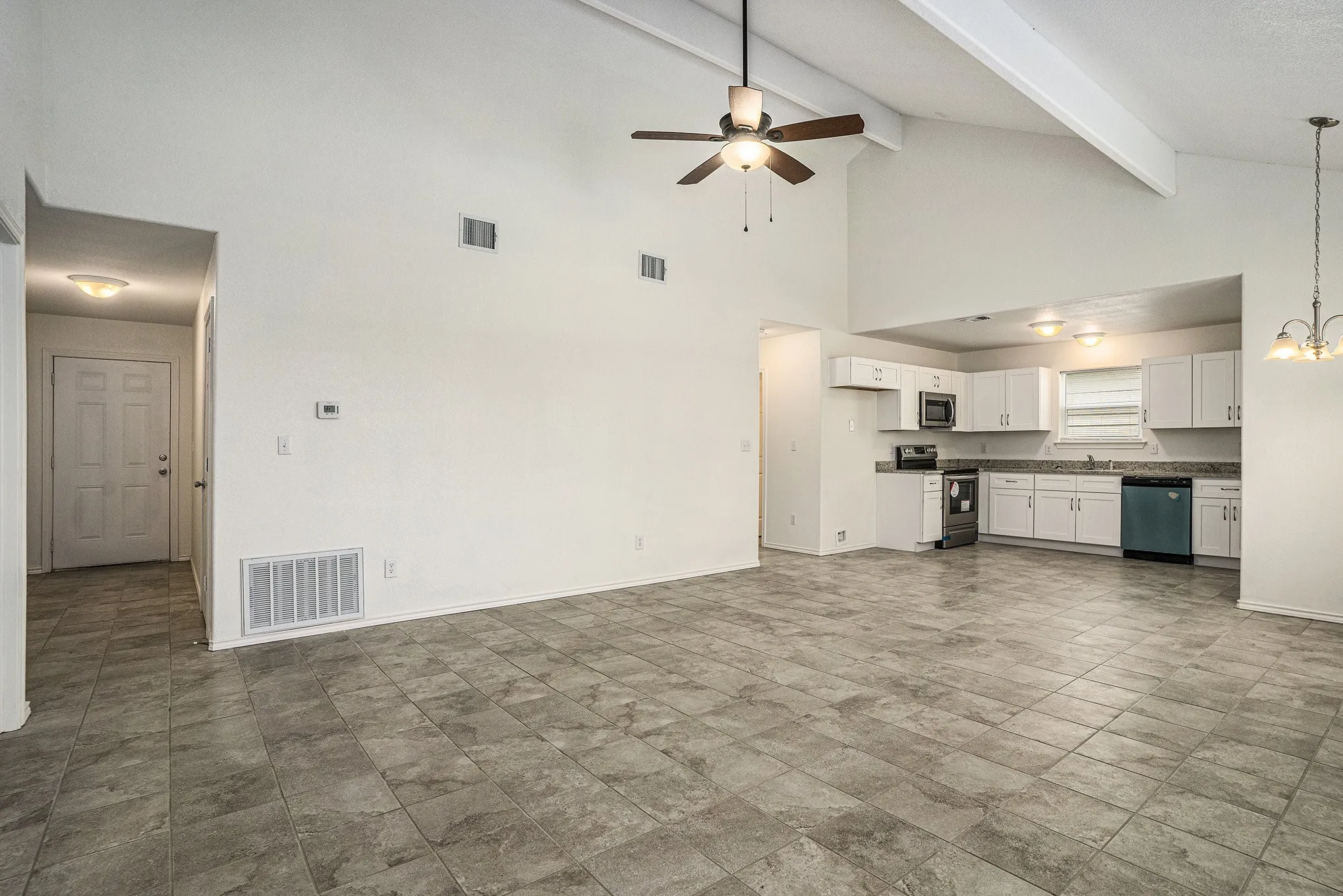Vaulted ceiling with exposed beams, ceiling fan, tile flooring, built-in kitchen cabinetry, and pendant light fixture