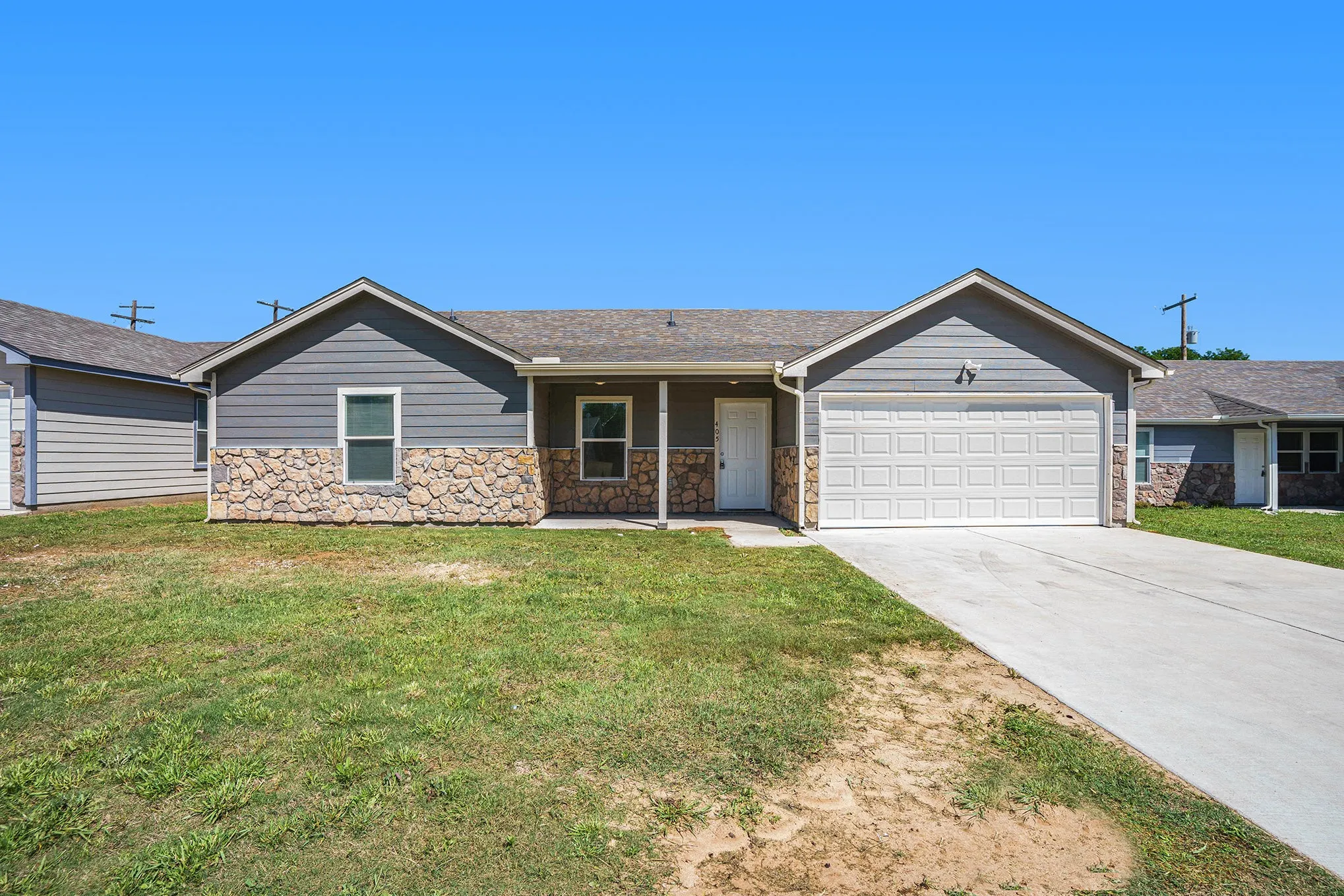 Single-story residence featuring a partial stone facade, gray siding, a covered front entry, an attached garage, and a concrete driveway