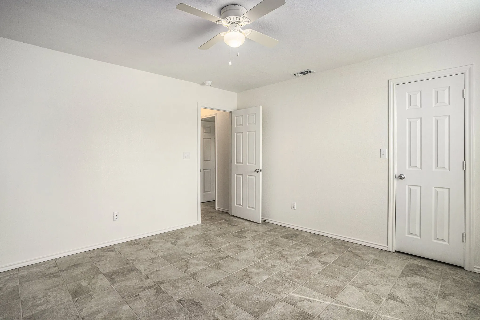 White walls, ceiling fan with integrated lighting, tile flooring, and multiple six-panel doors