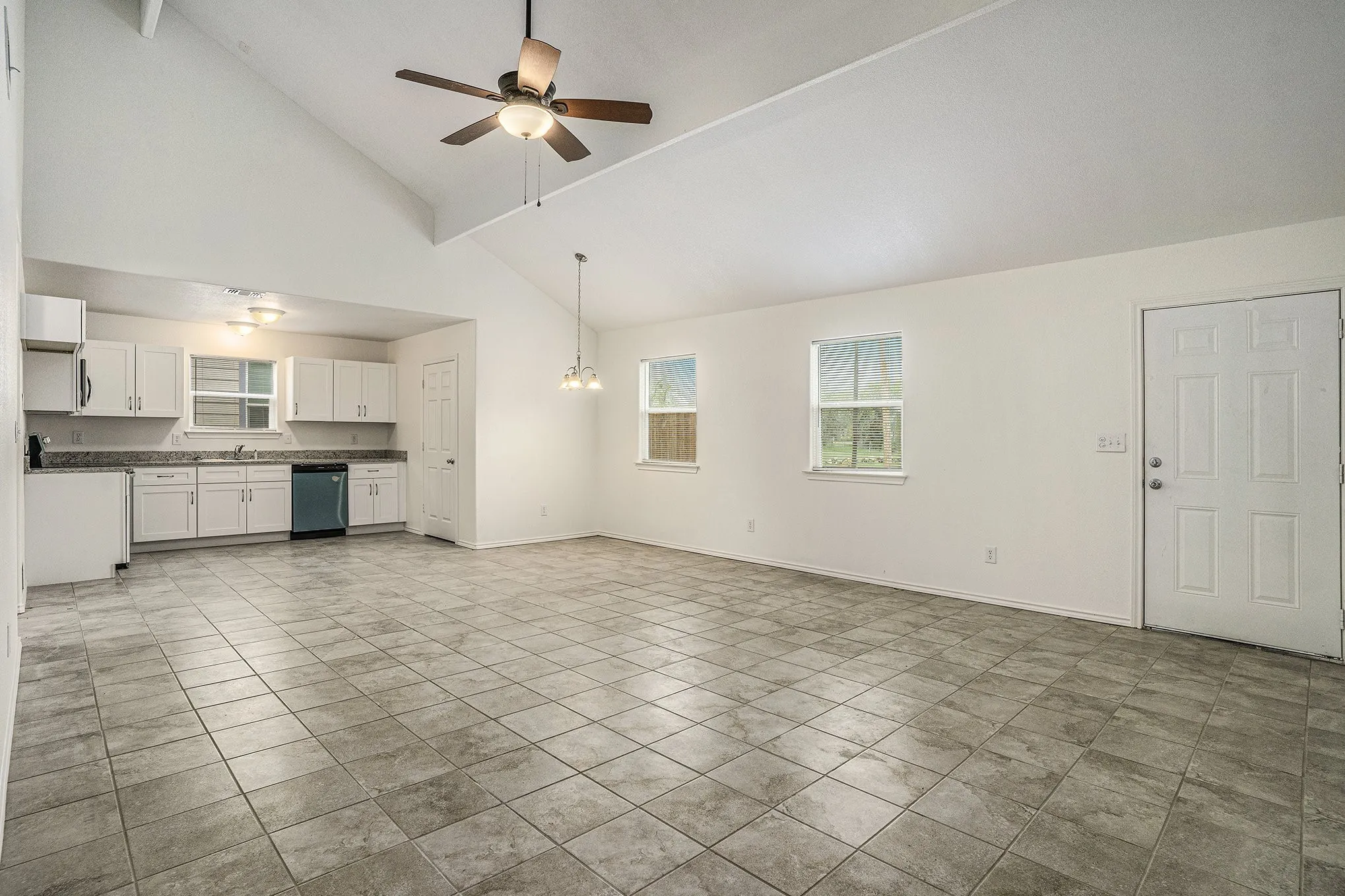 Vaulted ceiling with ceiling fan, tile flooring, white cabinetry, integrated dishwasher, and two windows