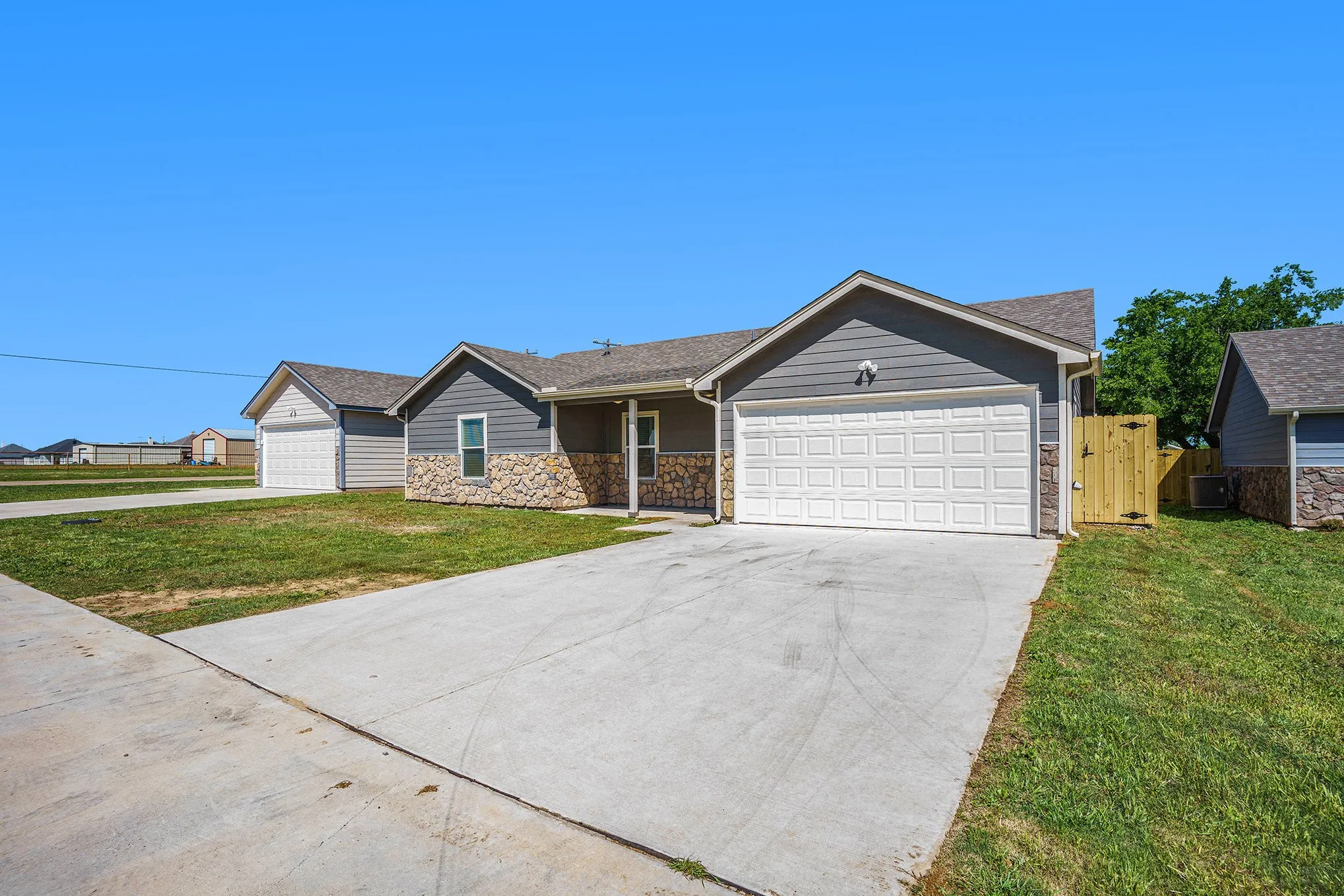 Property exterior featuring a gray siding facade, stone accents, attached garage, and a wooden privacy fence