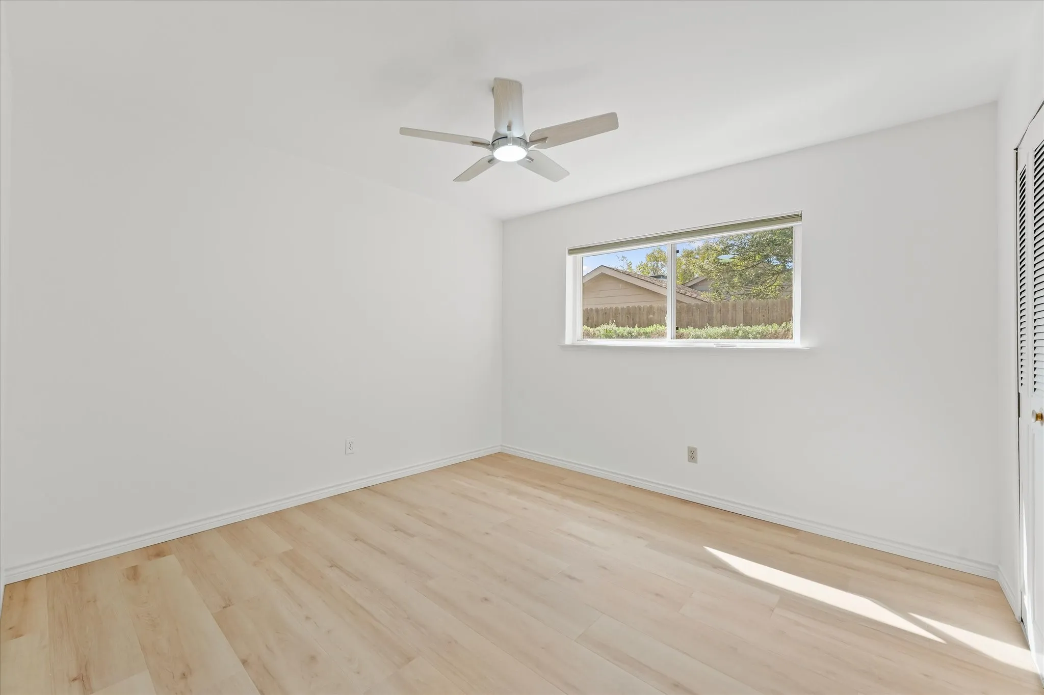 Room featuring light wood-finish LVP flooring, a neutral color palette, a brushed nickel ceiling fan with integrated lighting, a double-pane window, and louvered closet doors