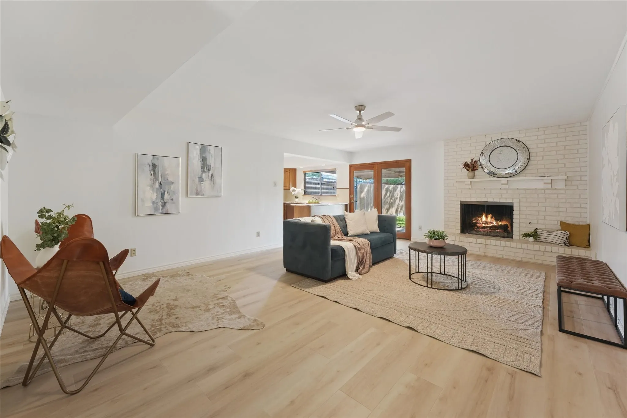 Expansive living area ready to entertain, featuring wood-finish LVP flooring, a white brick fireplace with a built-in hearth, a ceiling fan, and glass-paneled wooden exterior doors