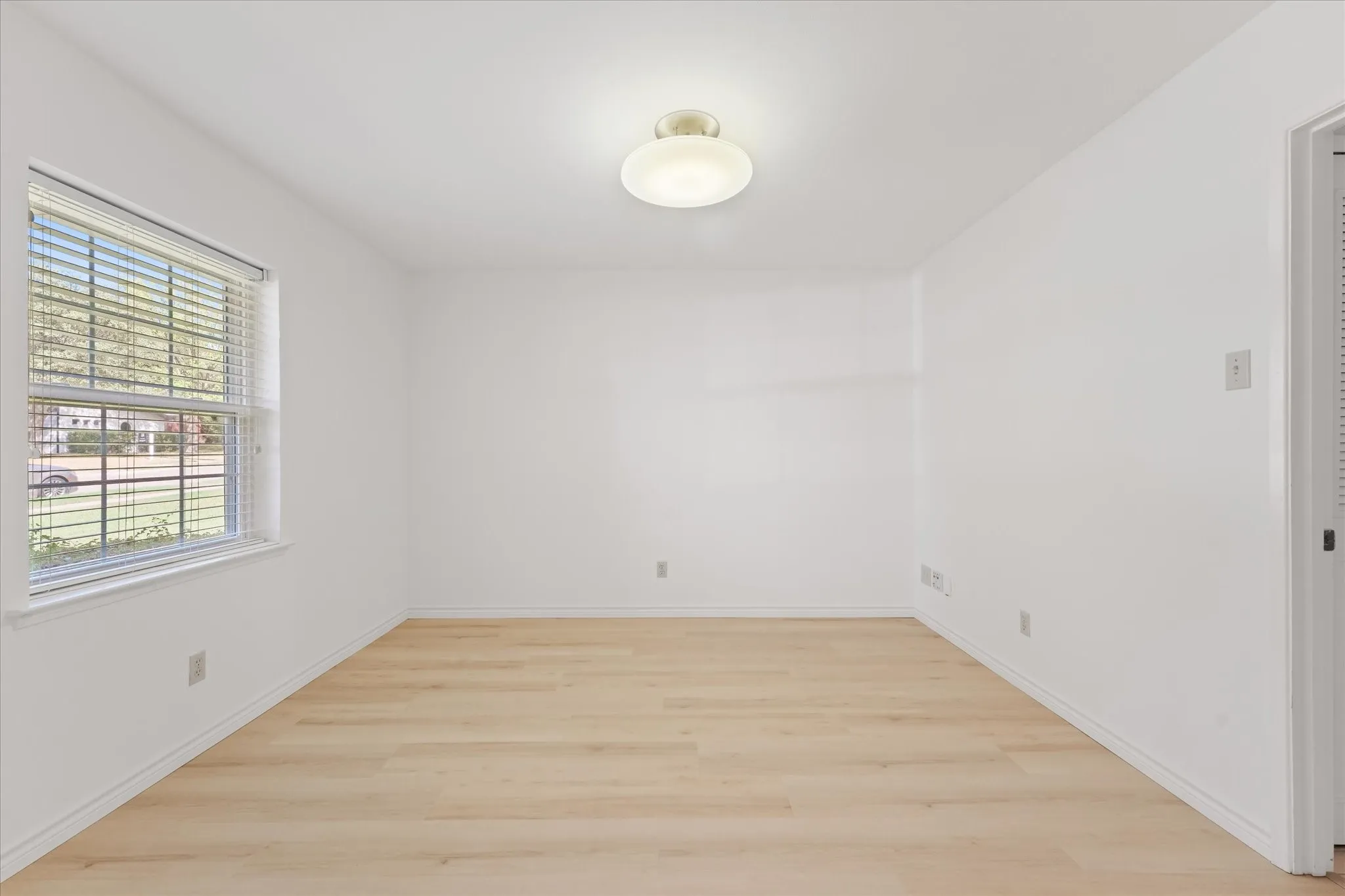 Interior space, perfect for office, featuring wood-finish LVP flooring, a neutral color palette, a multi-pane window with horizontal blinds, and a semi-flush mount ceiling fixture