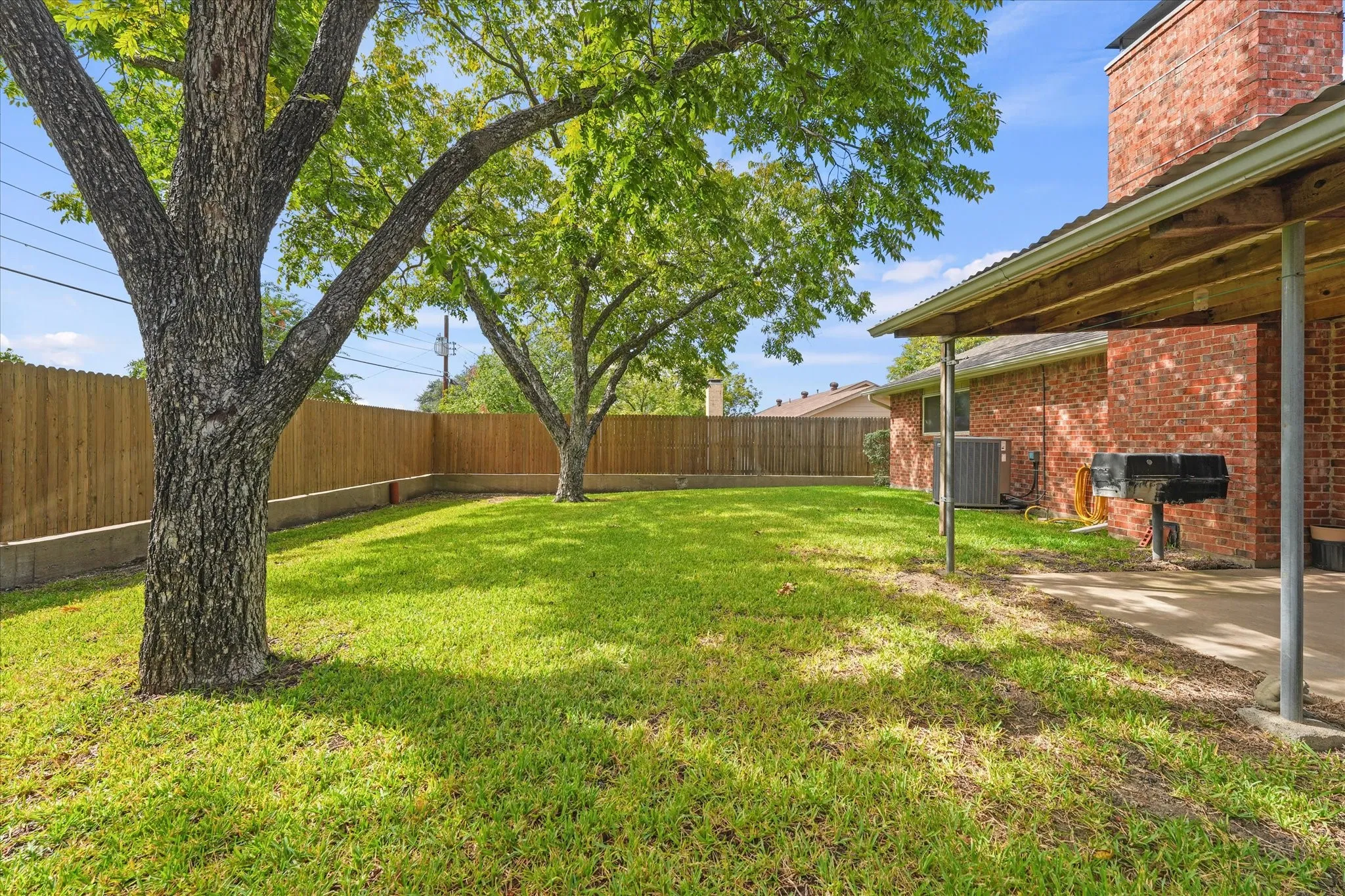 Private backyard featuring mature trees, a covered patio with a red brick exterior, and wood-style privacy fencing