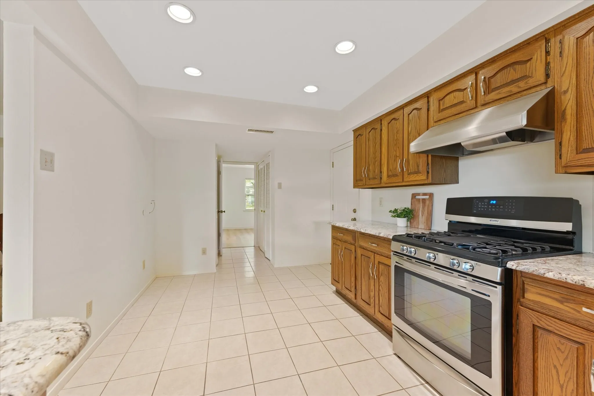 Eat in Kitchen featuring stained-wood cabinetry, stone-patterned countertops, stainless steel gas range, stainless steel range hood, and tile flooring