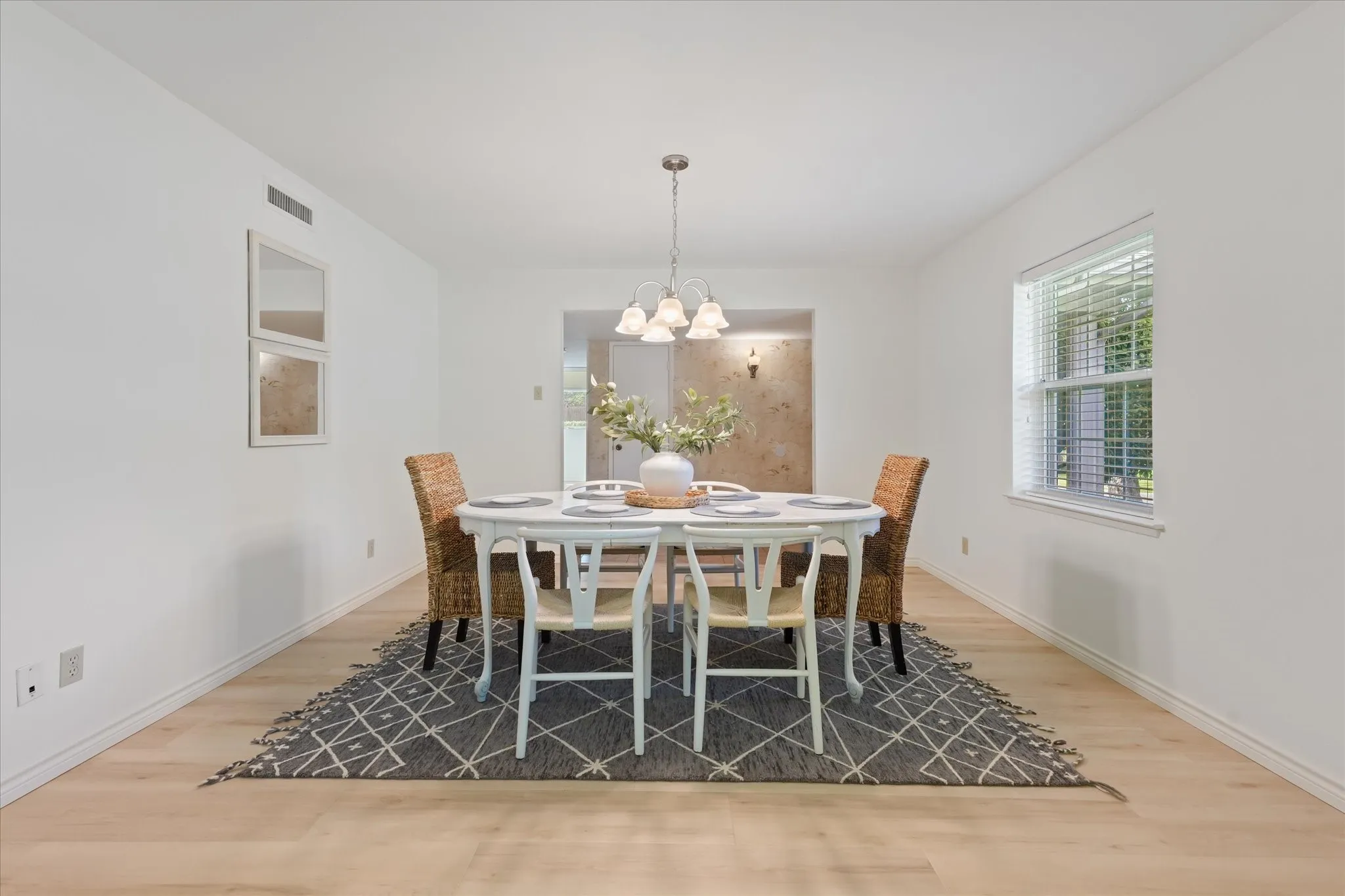 Dining space featuring light-toned wood-finish LVP flooring, a multi-bulb chandelier with frosted glass shades, and a double-pane window