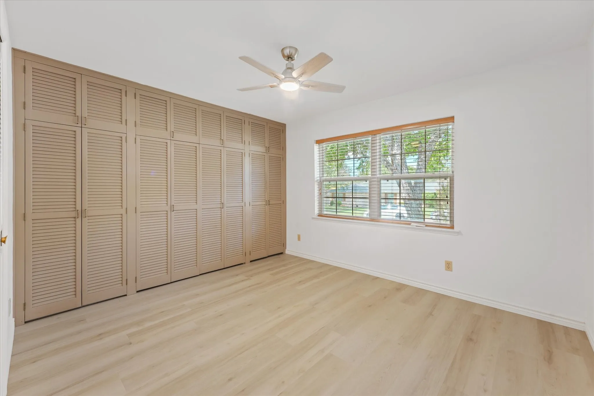Wall-to-wall built-in cabinetry featuring louvered doors, light-toned wood-finish LVP flooring, and a multi-blade ceiling fan with integrated LED lighting
