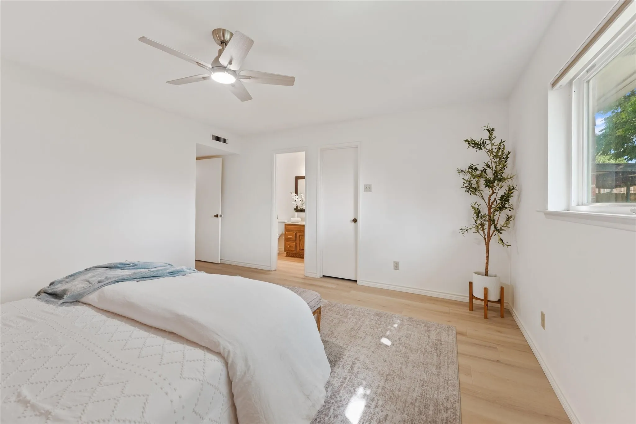 Neutral interior featuring light-tone wood-finish LVP flooring, white walls, a flush-mount ceiling fan with integrated lighting, and a double-pane window with influx of natural light